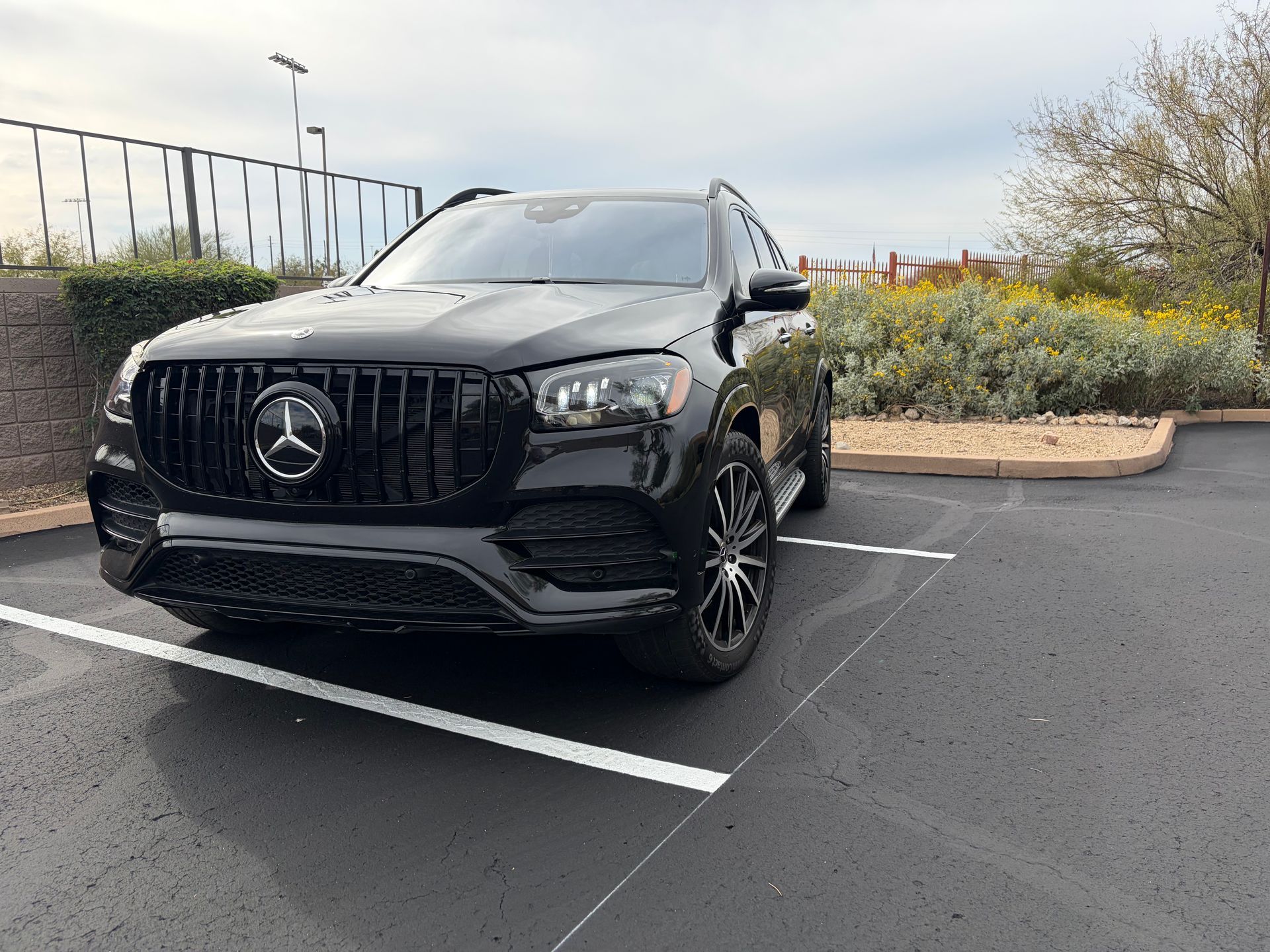Black Mercedes SUV parked in a striped lot near yellow flowers and a cloudy sky