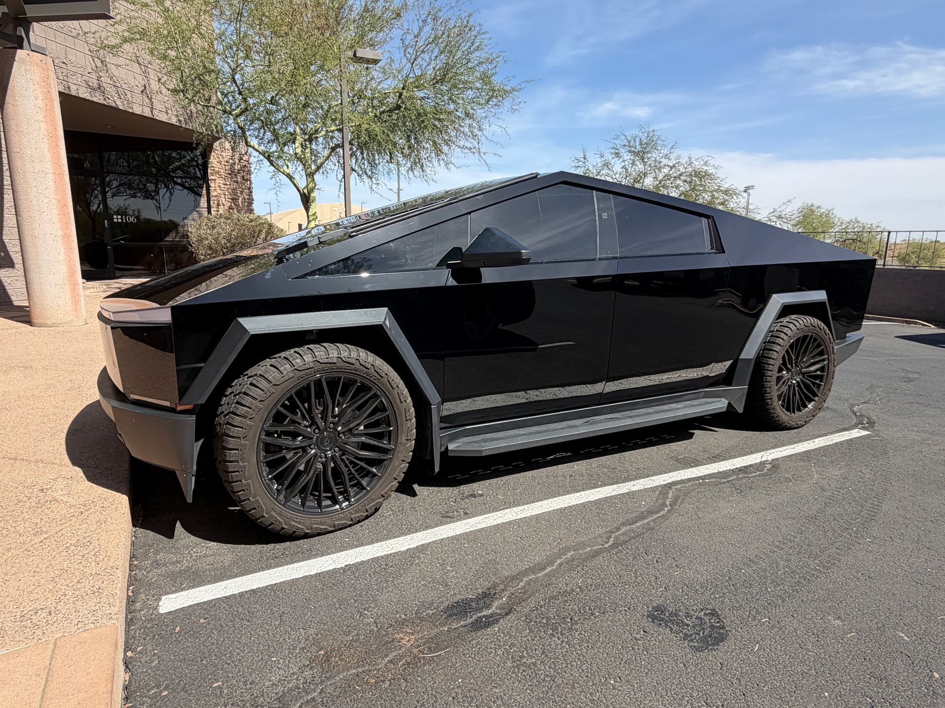 Black angular electric truck parked in a lot beside a building, with tinted windows and custom wheels