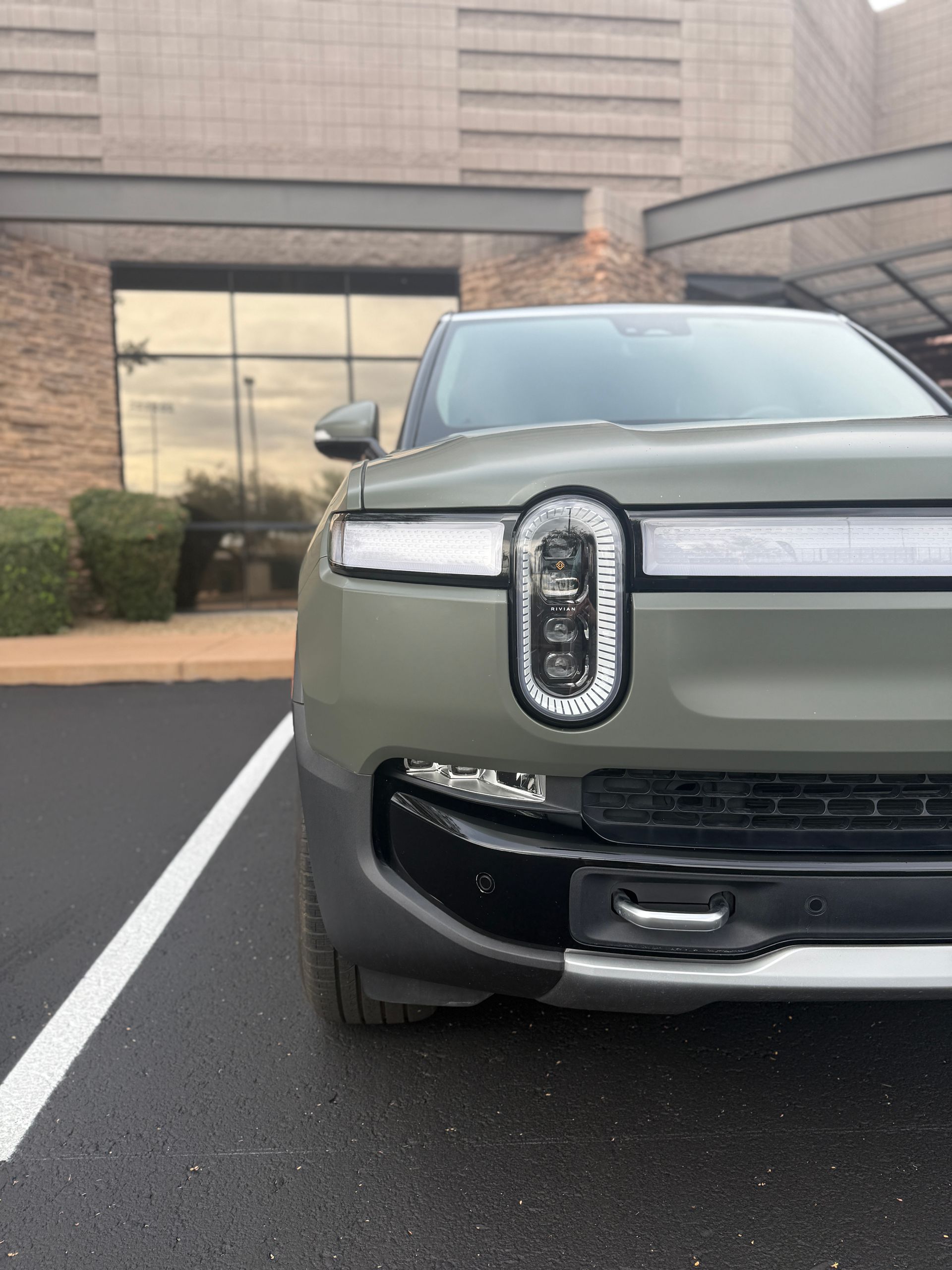 Front view of a gray Rivian SUV parked in a lot beside a building.
