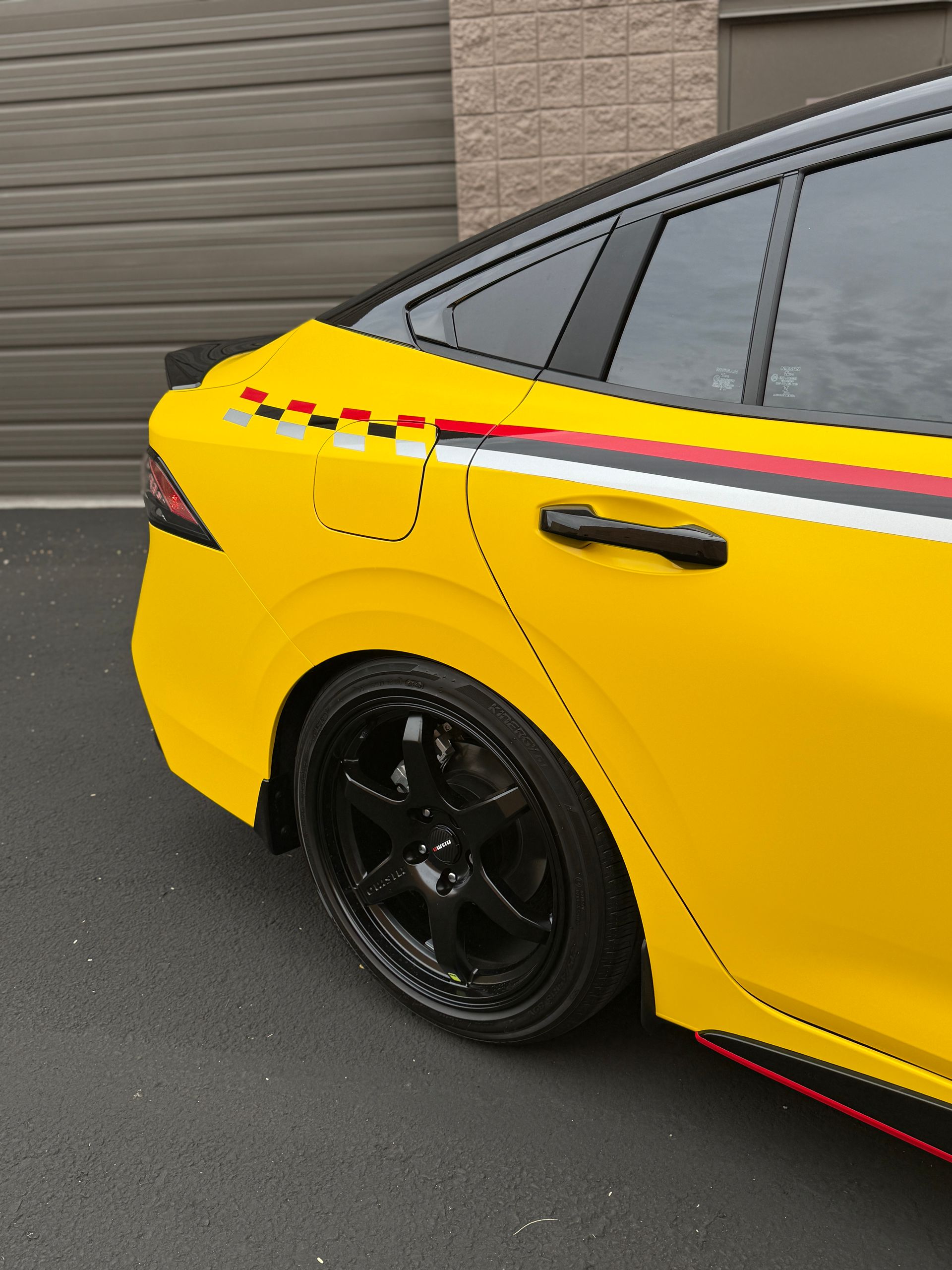 Yellow sedan with black wheels and red stripe parked near a garage door