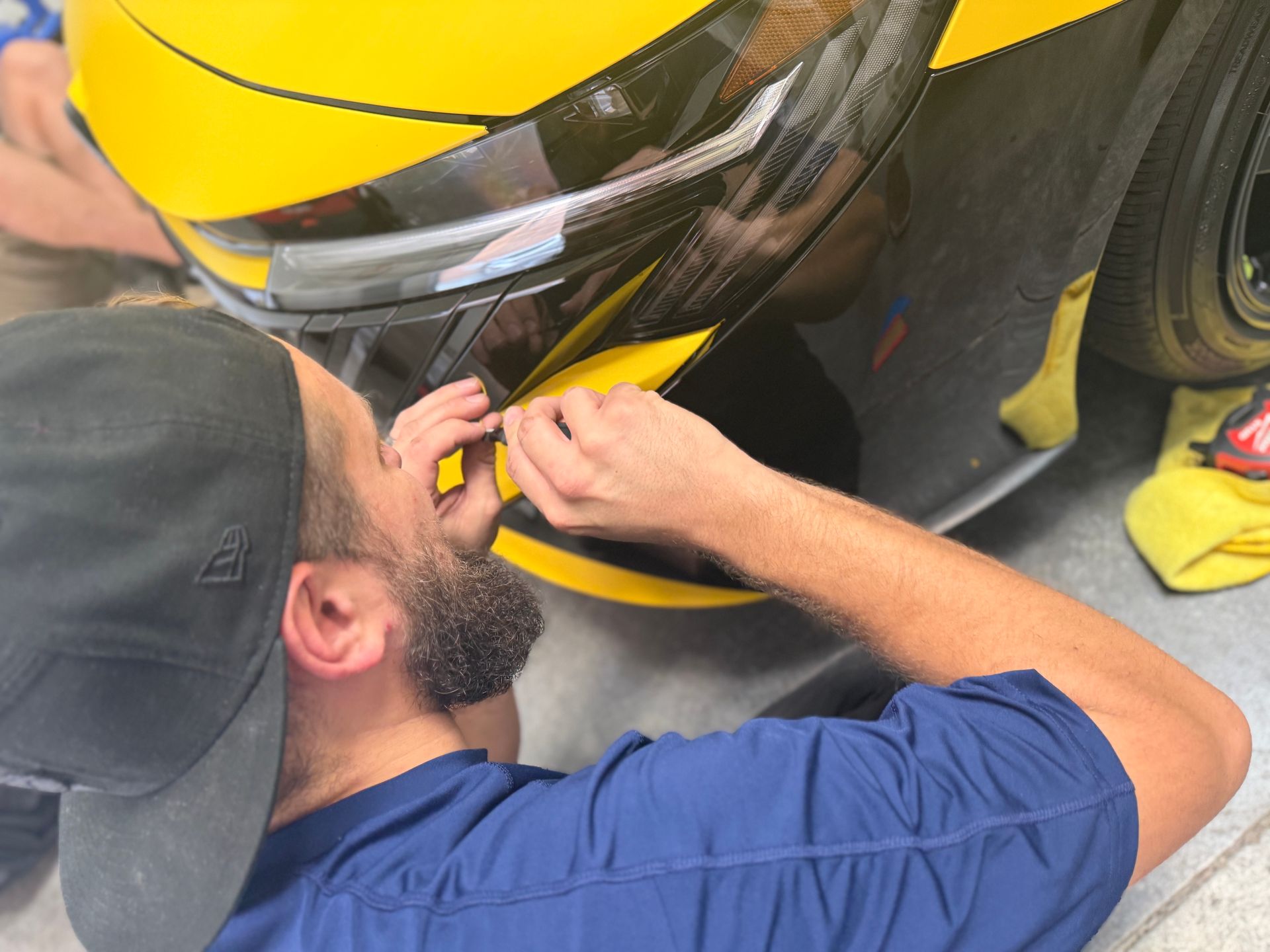 Mechanic working on a yellow car’s front bumper with tools close-up