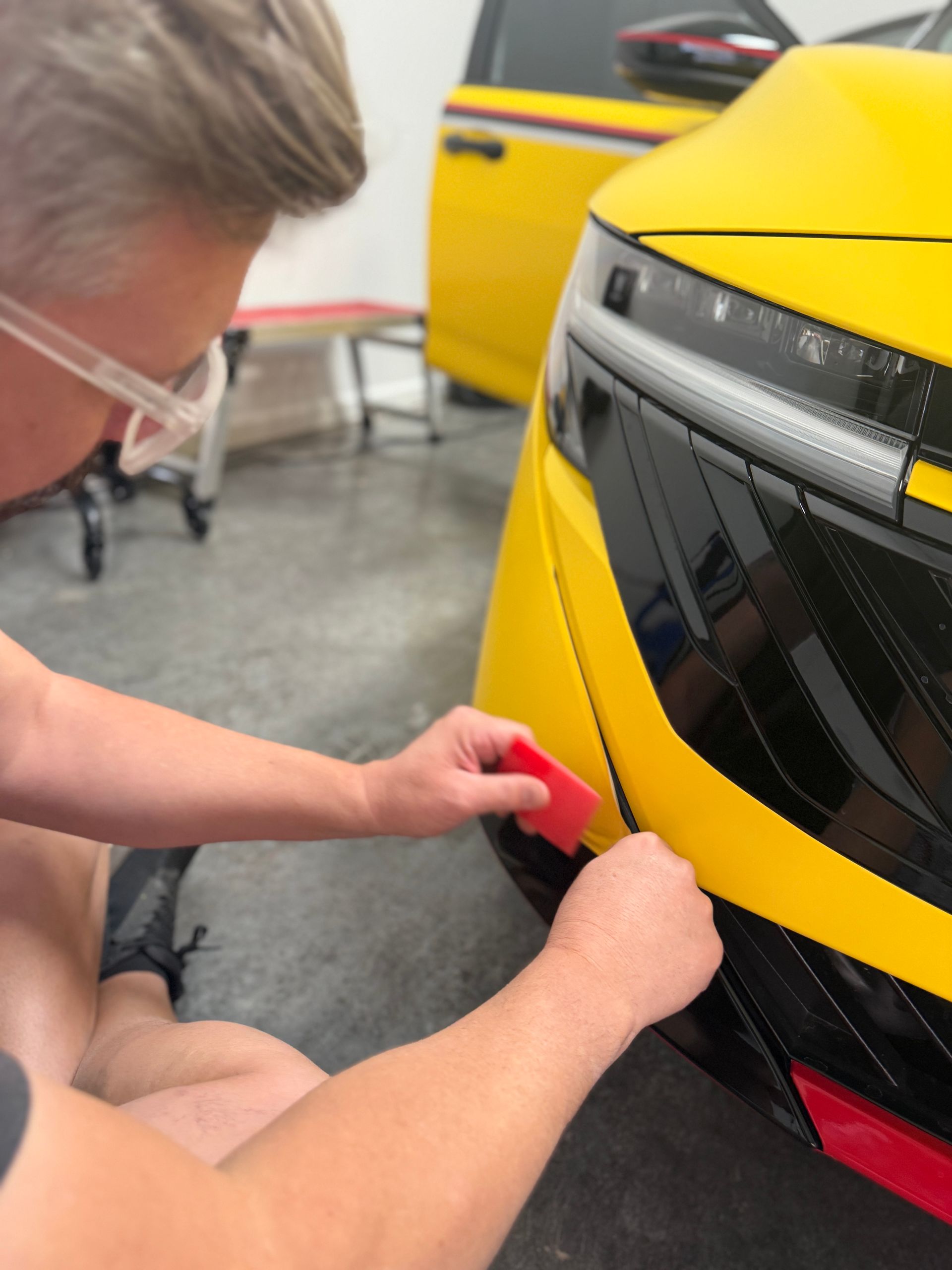 Person applying red tape to the front of a yellow car