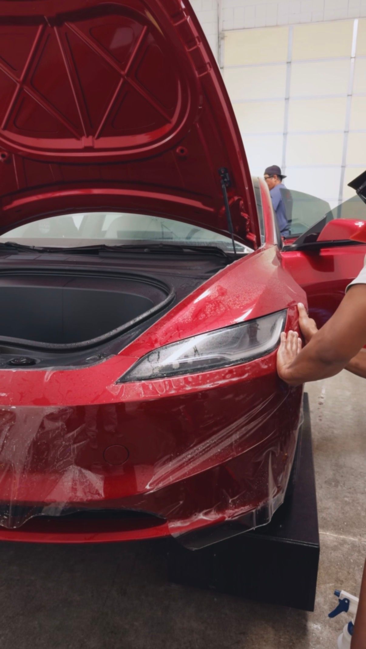 Red sports car with hood open, showing the front-left headlight in a garage.