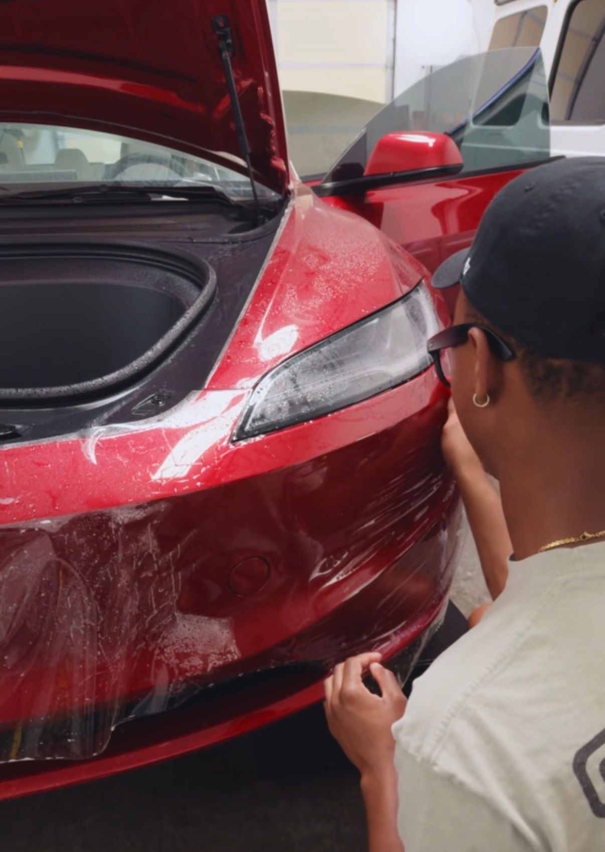 Person applying clear film to red car near open trunk and headlight