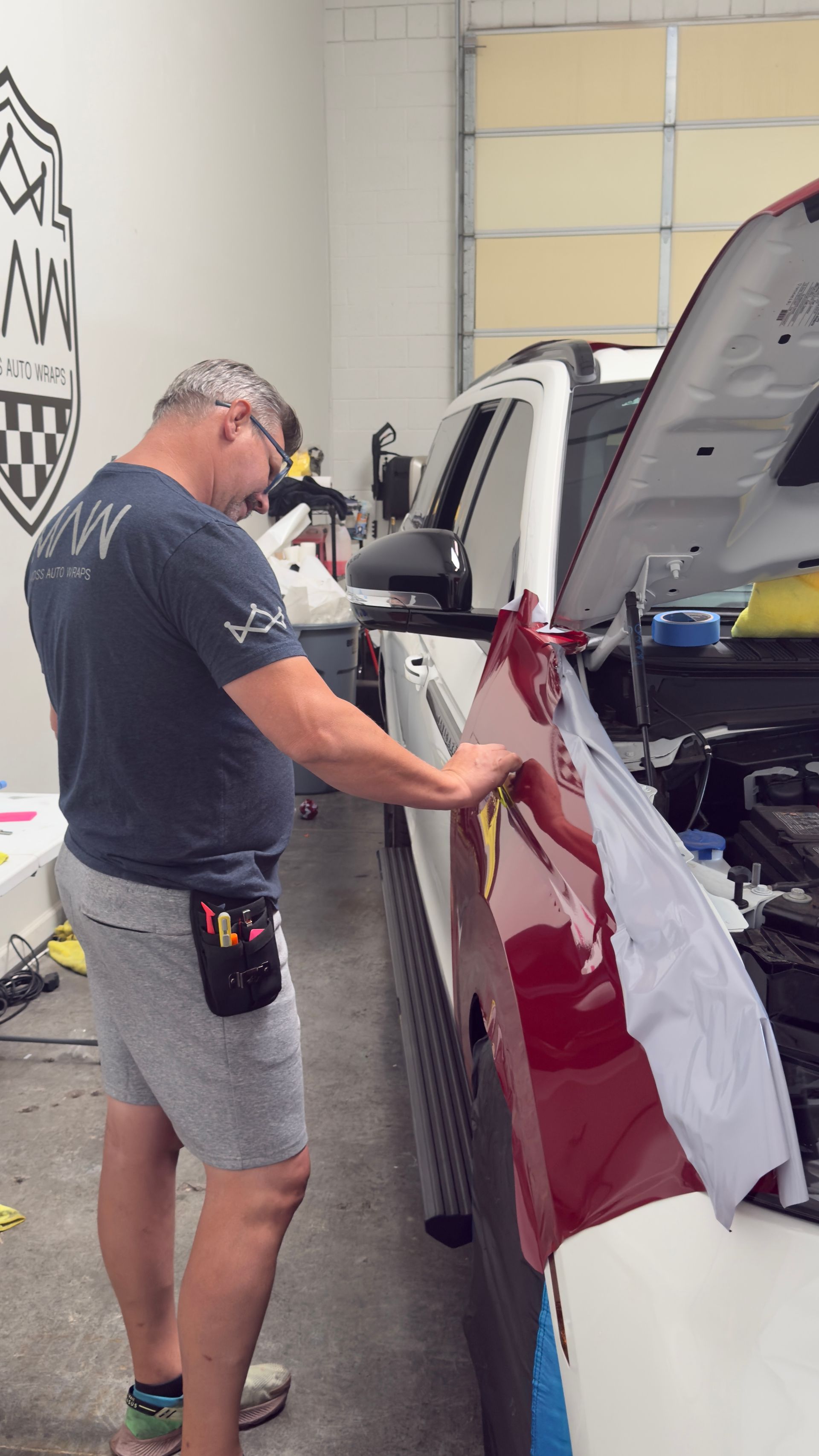 Man inspecting a red and white vehicle inside a garage with the hood open