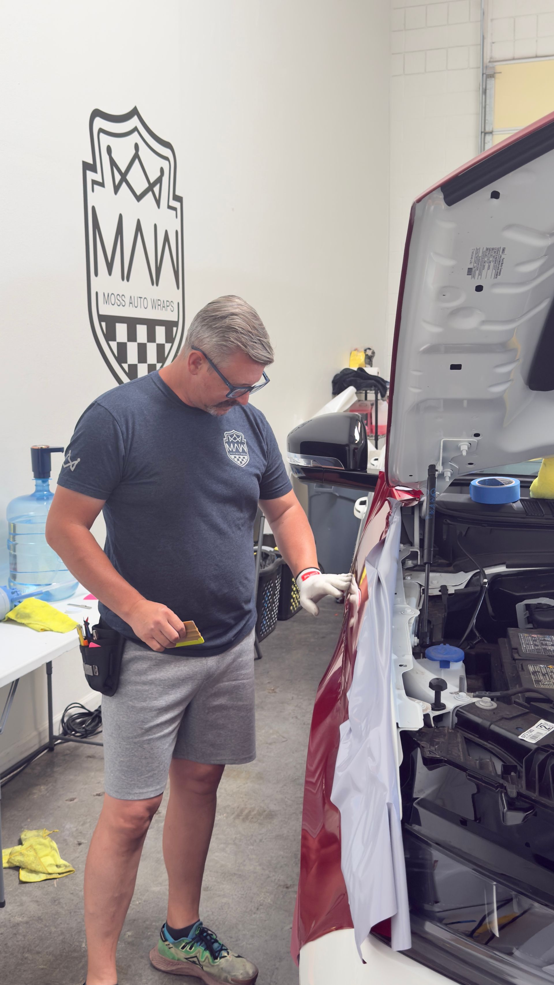 Man standing in a shop, looking down at a large open machine or display with tools nearby.