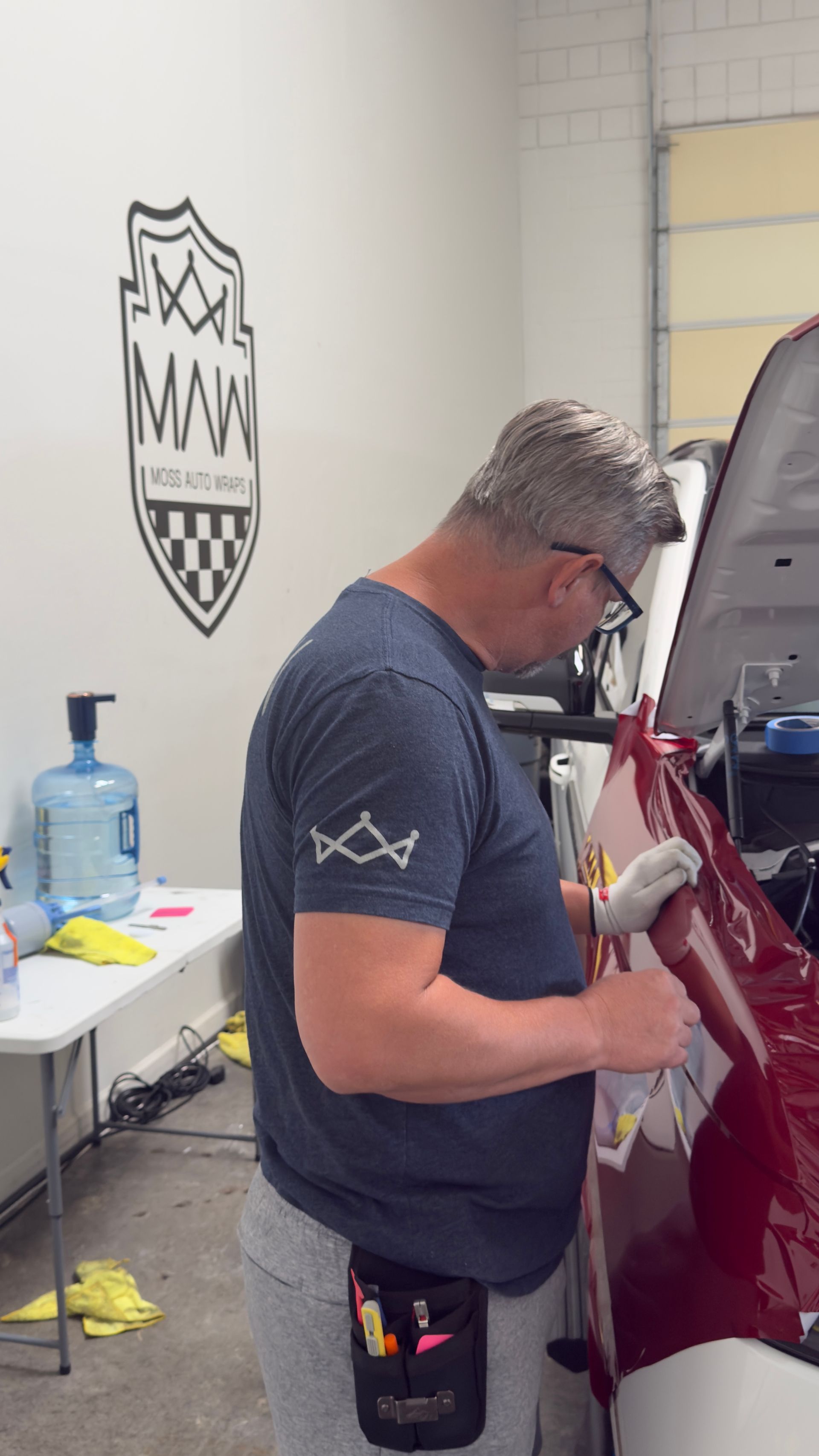 Technician polishing a maroon car in a garage workshop