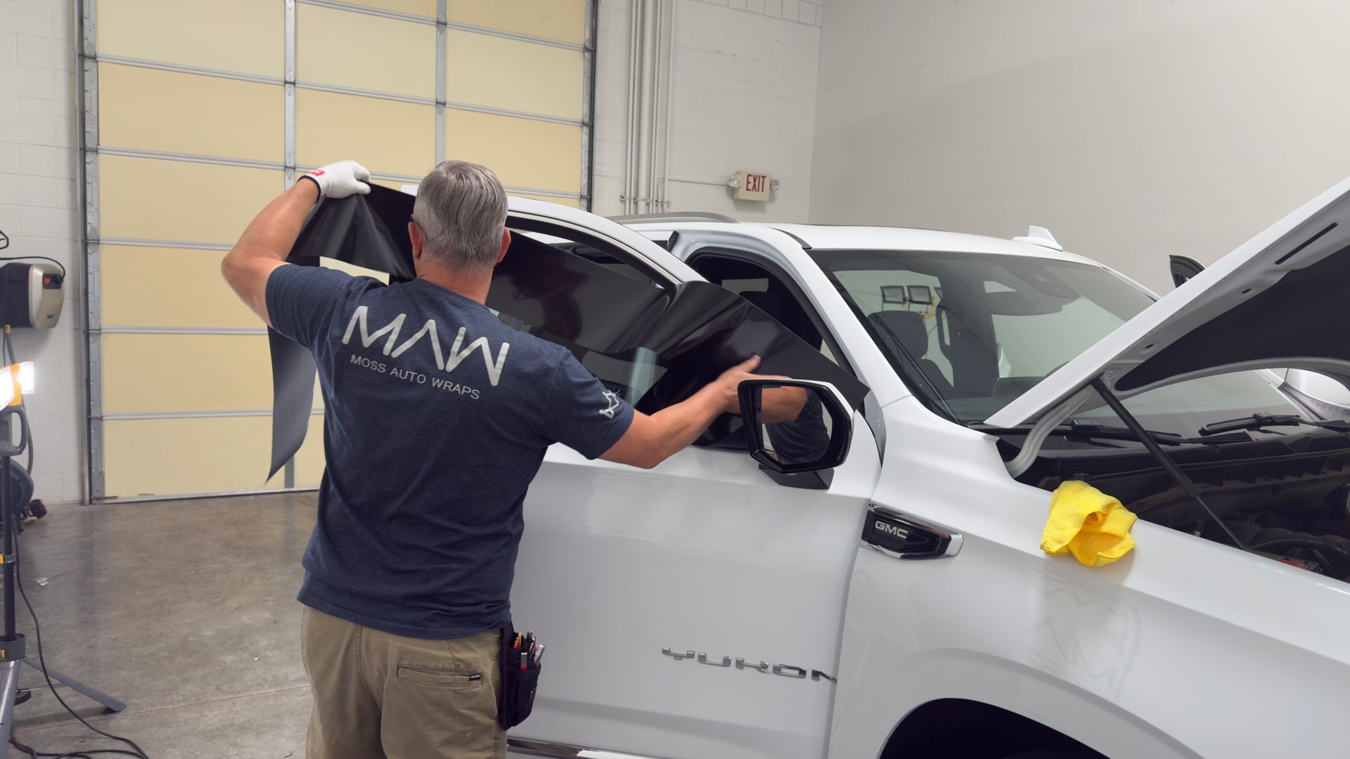 Man cleaning a white pickup truck in a garage, wiping the windshield and side mirror with a cloth