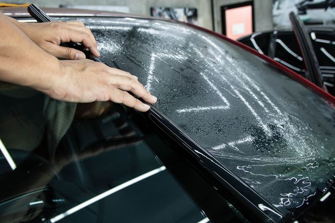 Hands peeling protective film from a car windshield in a garage