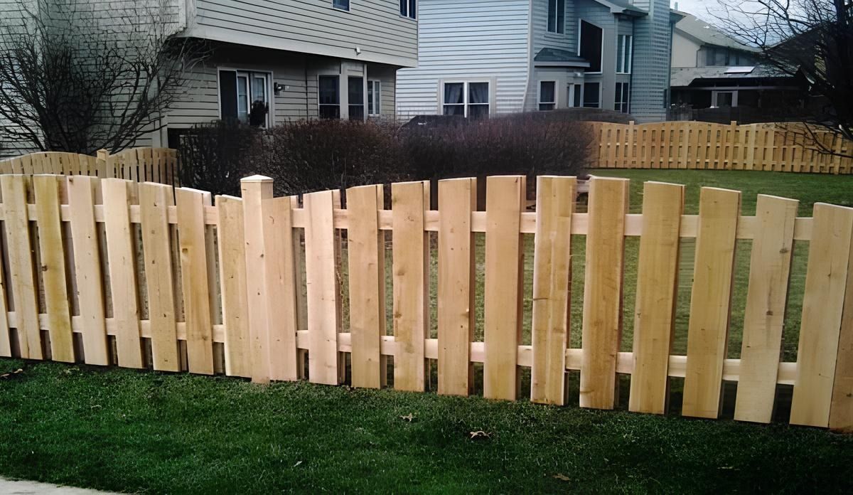 Wooden picket fence in front of a green lawn, with houses in the background.