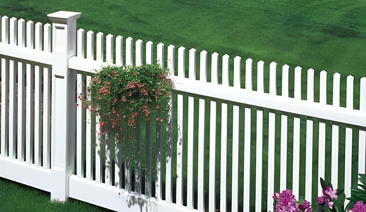White picket fence with a hanging flower basket in front of green grass.