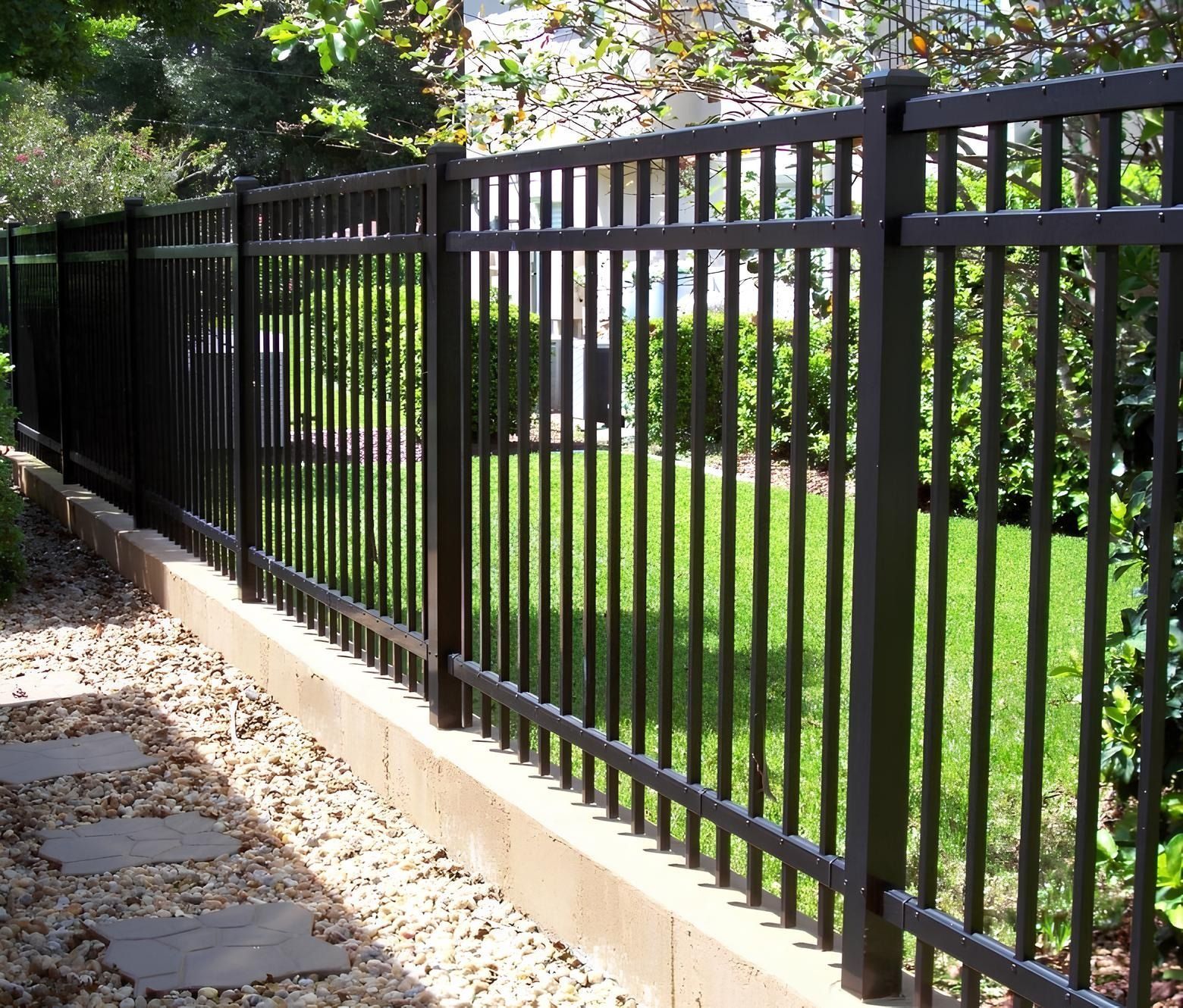 Black metal fence bordering a grassy yard, with a stone path and a few shrubs.