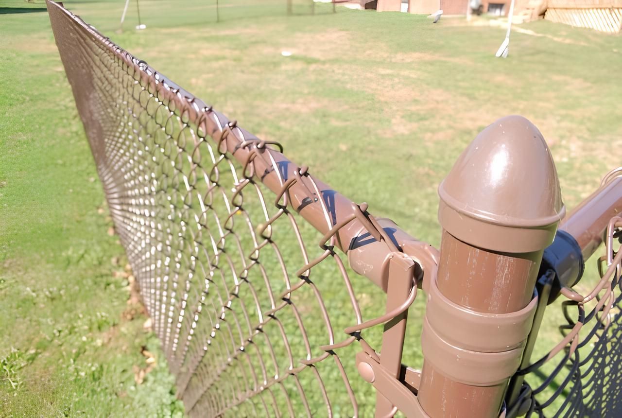 Brown chain-link fence in front of a grassy field, with a brown post in the foreground.
