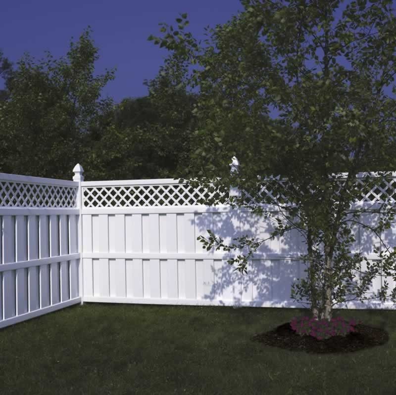 White vinyl fence in a grassy yard, with a tree casting a shadow and dark green trees in the background.