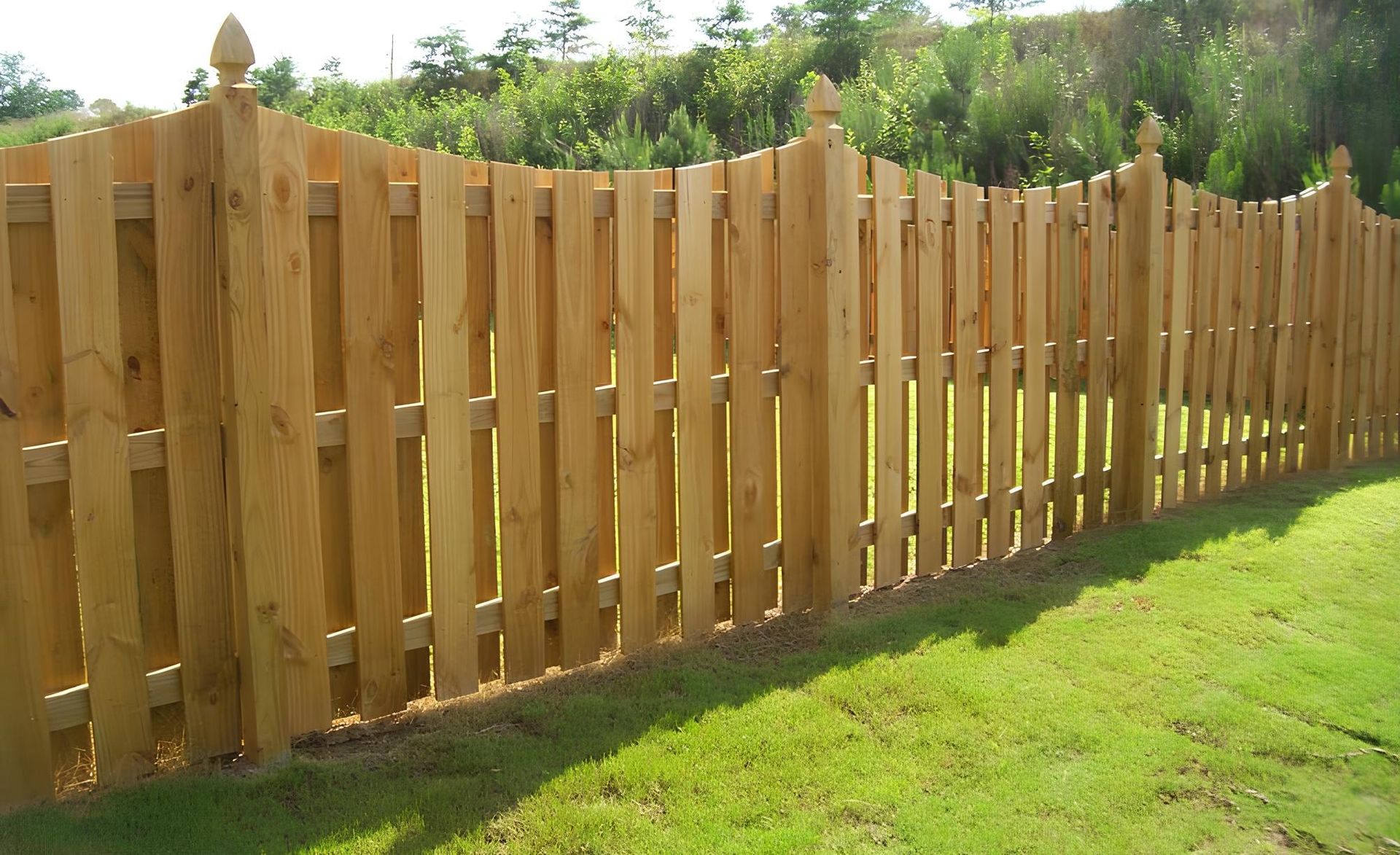 Wooden fence in a grassy yard, with a decorative top and finials.