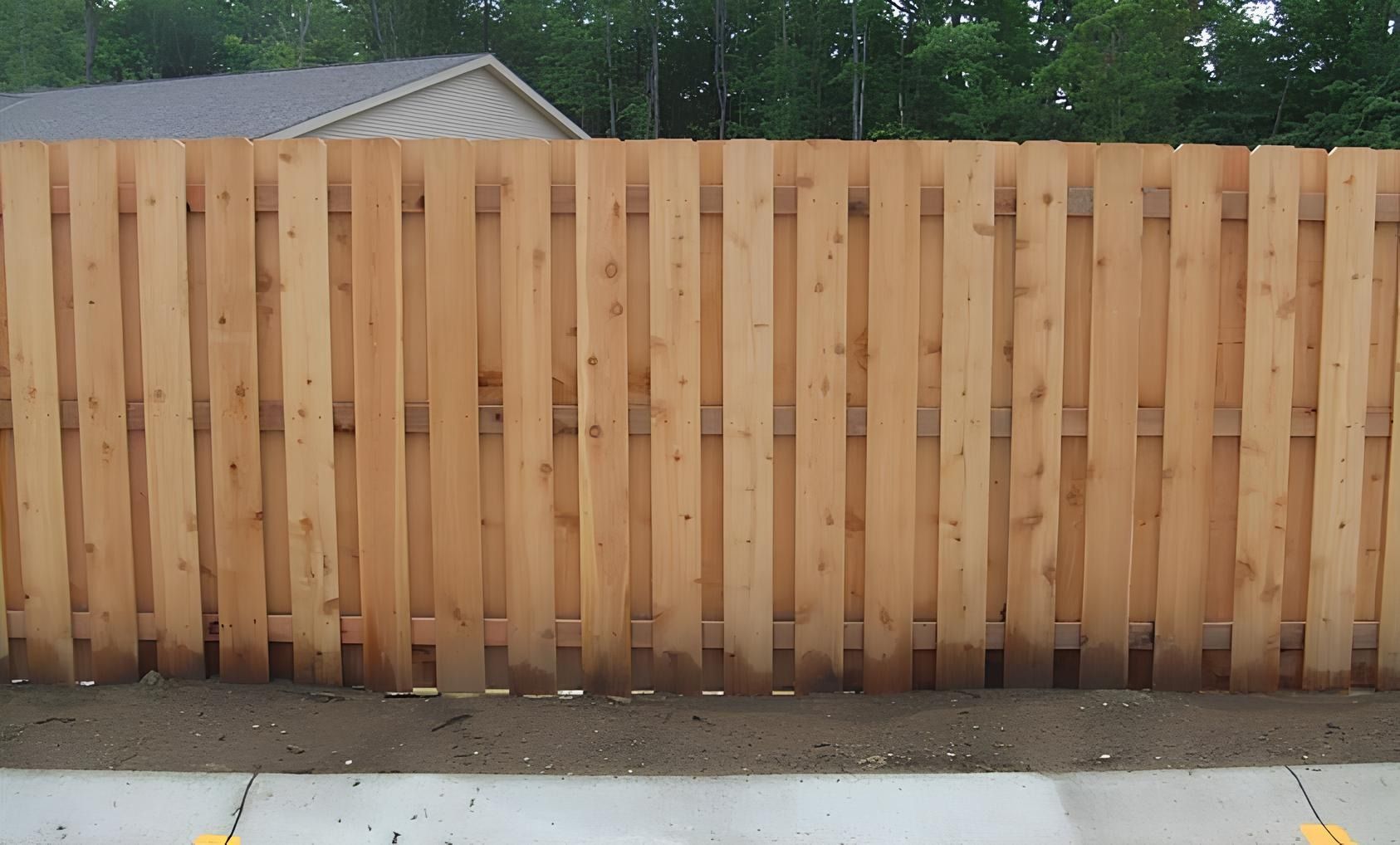 Wooden privacy fence in a suburban setting, with a gray concrete curb in the foreground.
