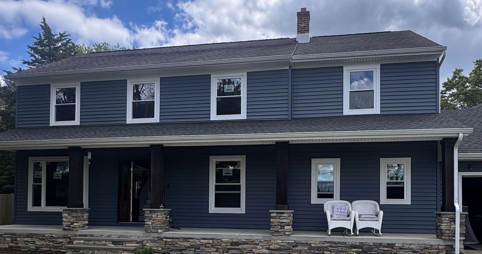 Two-story blue house with white-trimmed windows and a front porch with stone pillars.