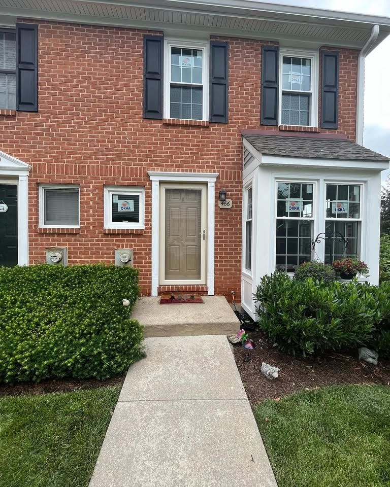 Brick townhouse with black shutters, a tan door, and a walkway.