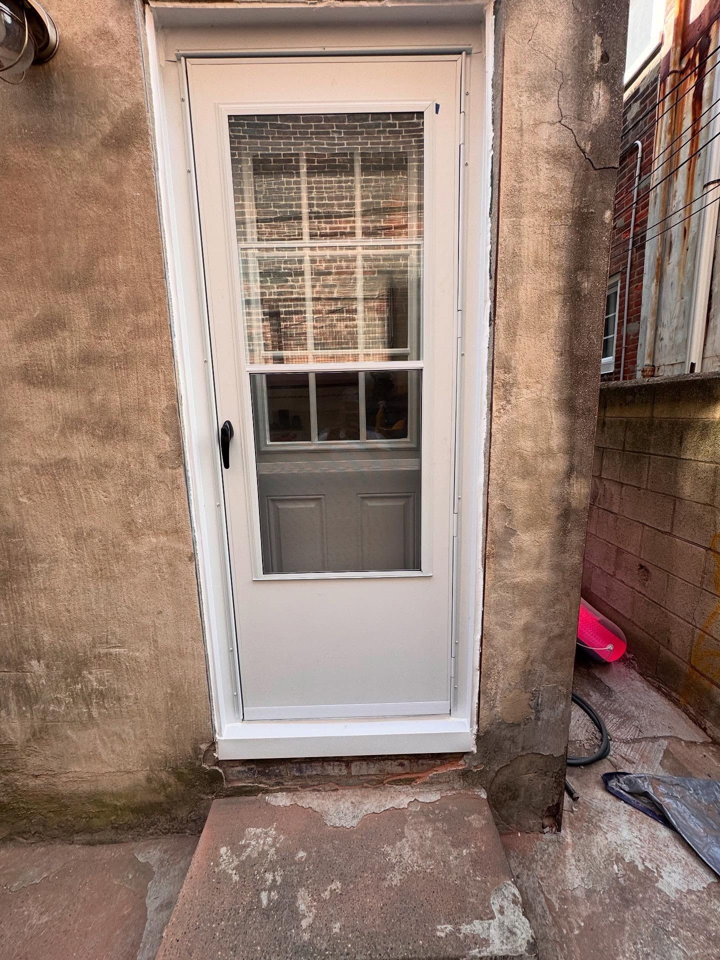 White door with glass pane and storm door, set in a weathered, uneven concrete wall.