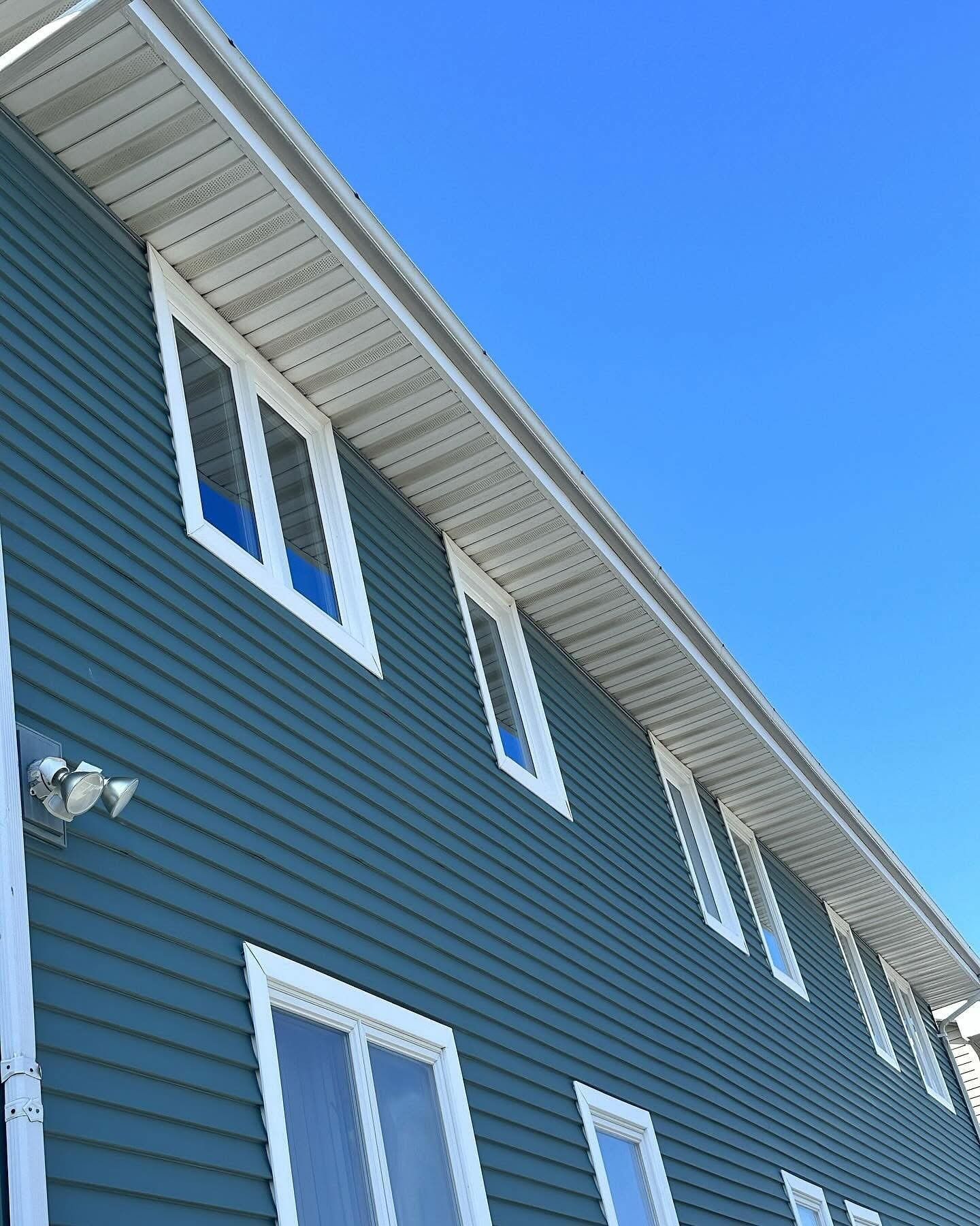 Blue siding building with white window frames and trim against a clear blue sky.