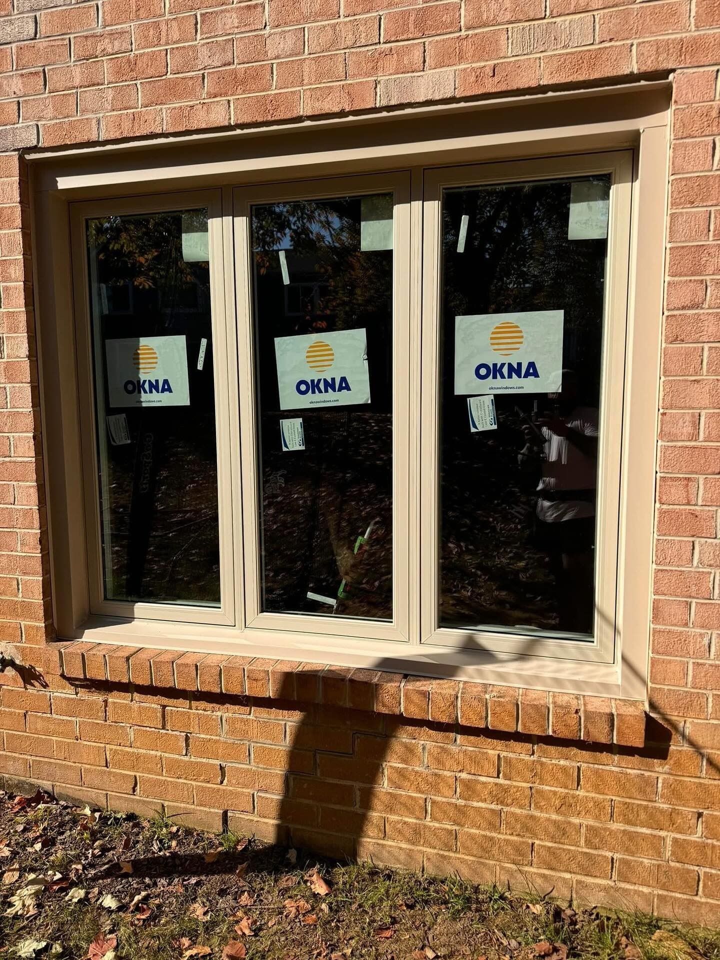 Brick building with a three-panel window. Tan frame, dark glass, protective stickers visible.