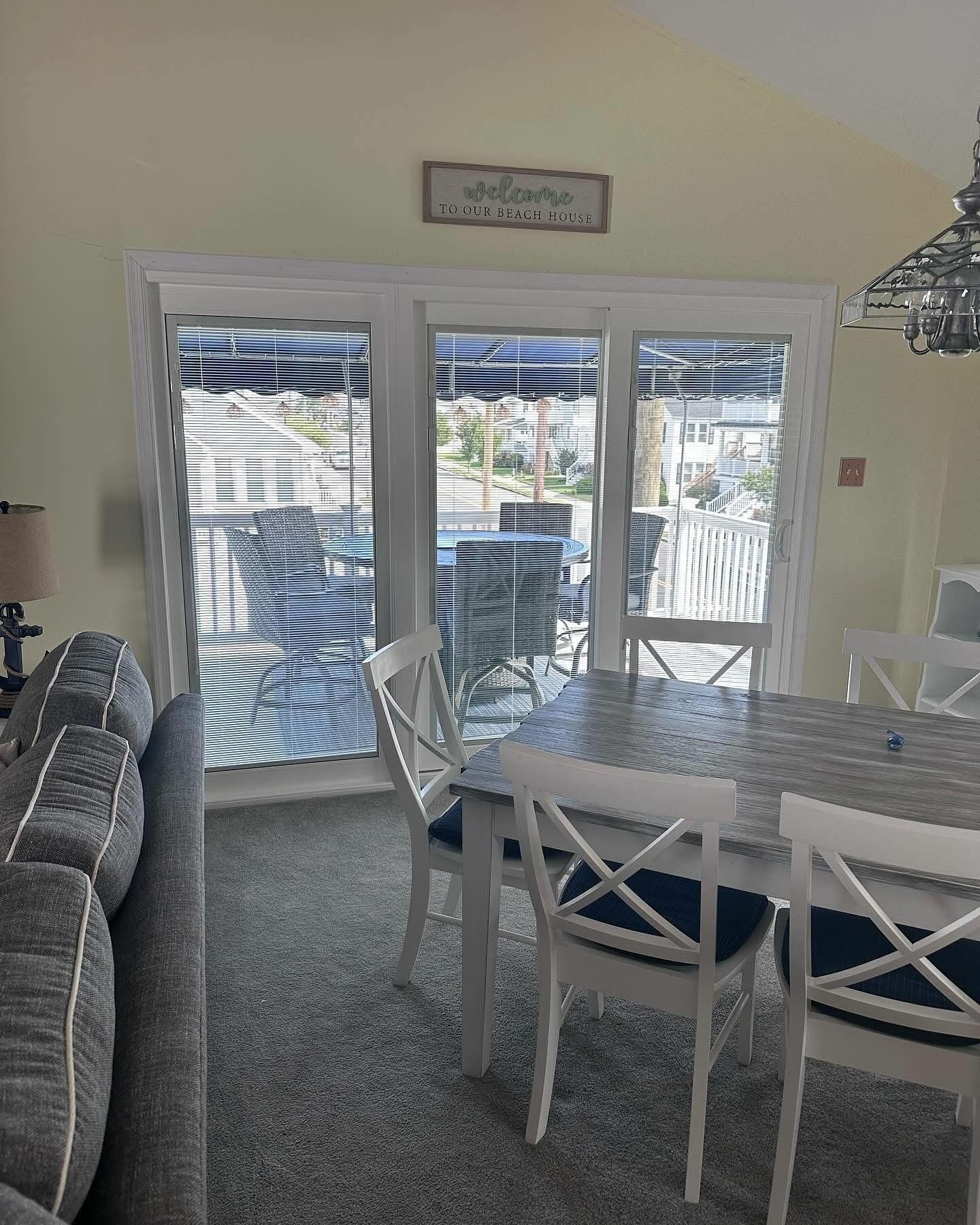 Dining area with white table and chairs, sliding glass doors, and a welcome sign.