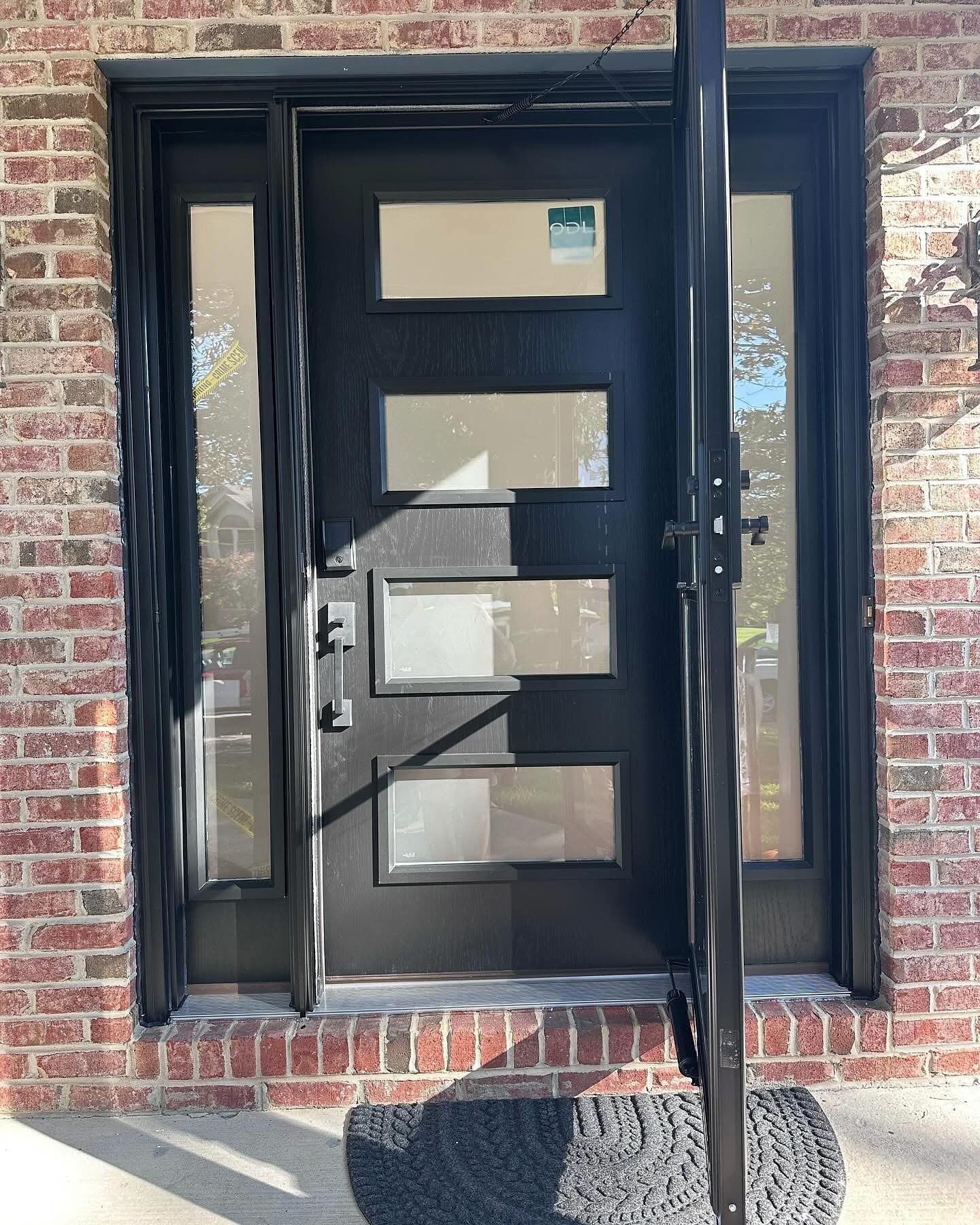 Black front door with rectangular windows, flanked by sidelights, set in brick.