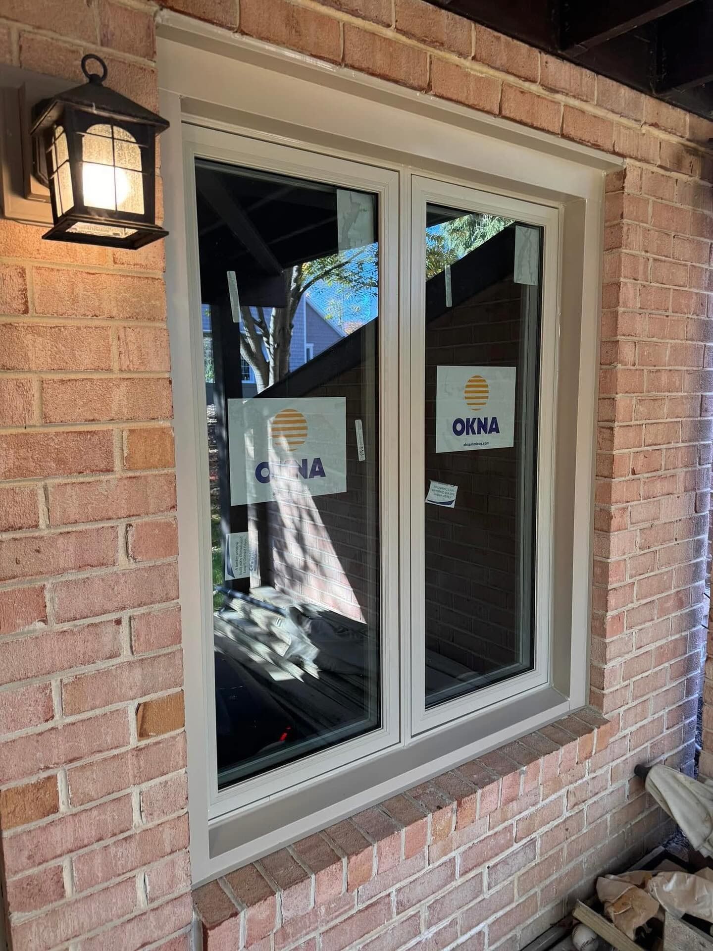 A new window installed on a brick building with tan trim. A lit lantern hangs nearby.