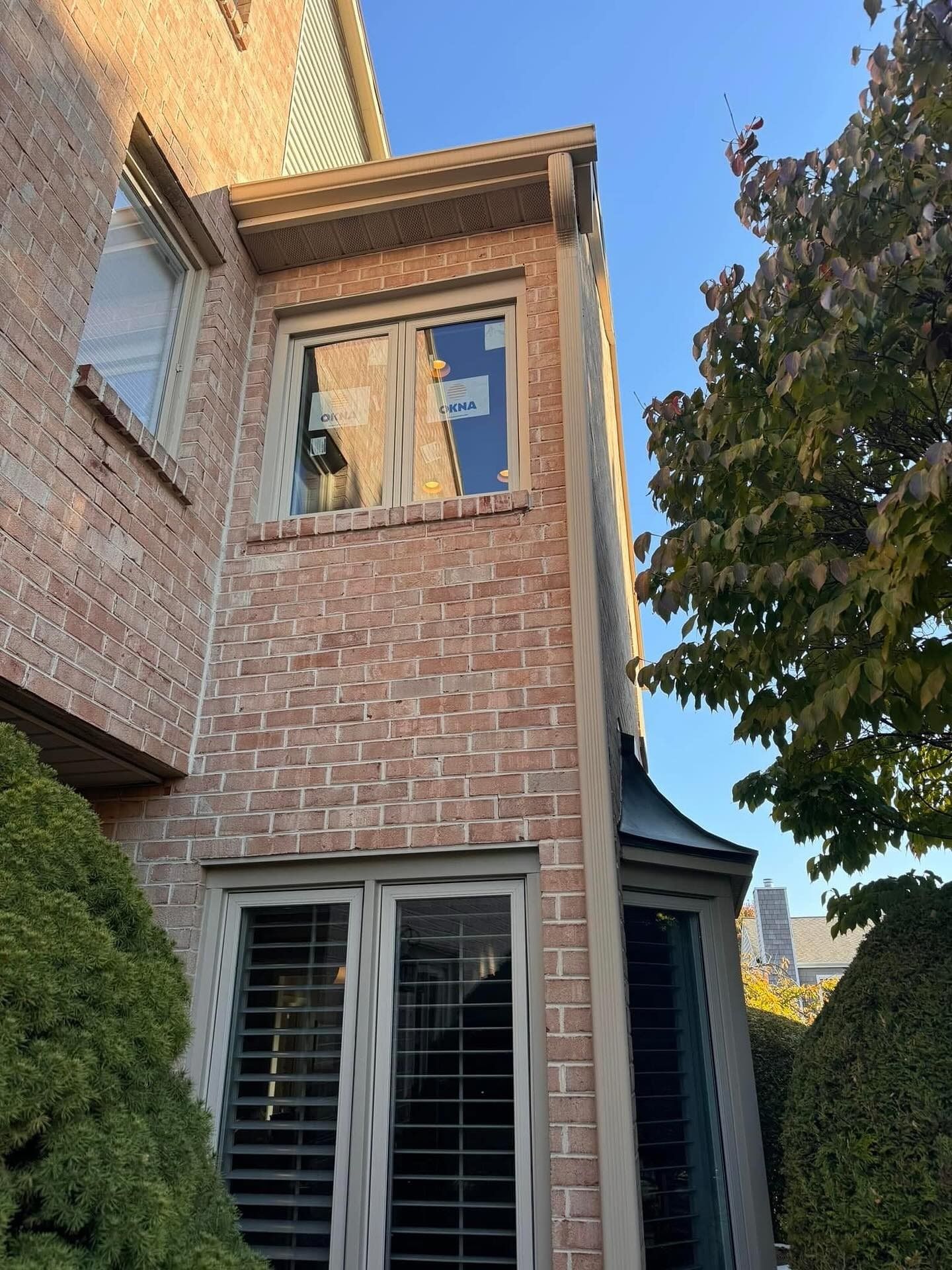 Brick building exterior with window and trees under a clear blue sky.