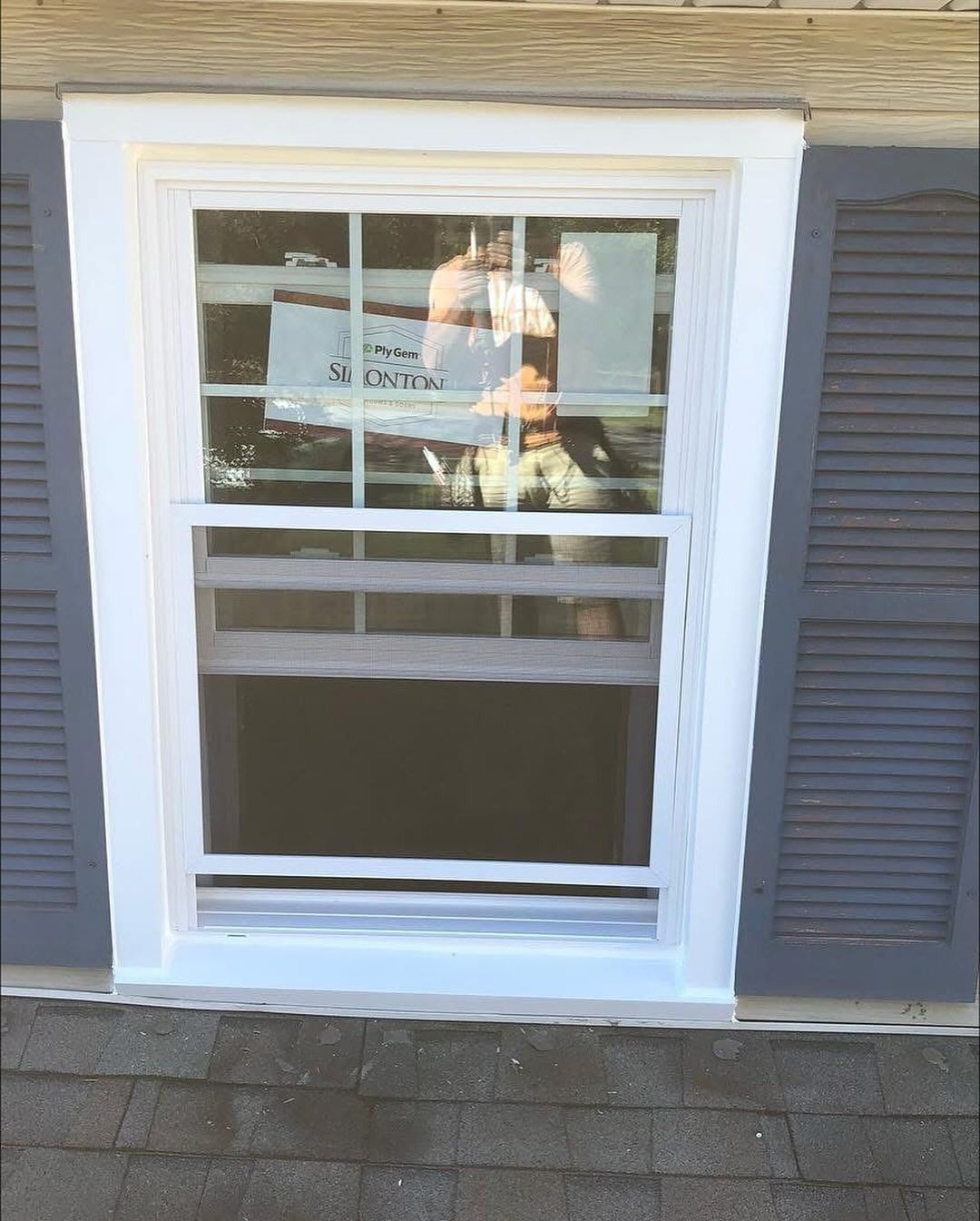 White-framed window with gray shutters. Open interior visible, with a sign in the window.