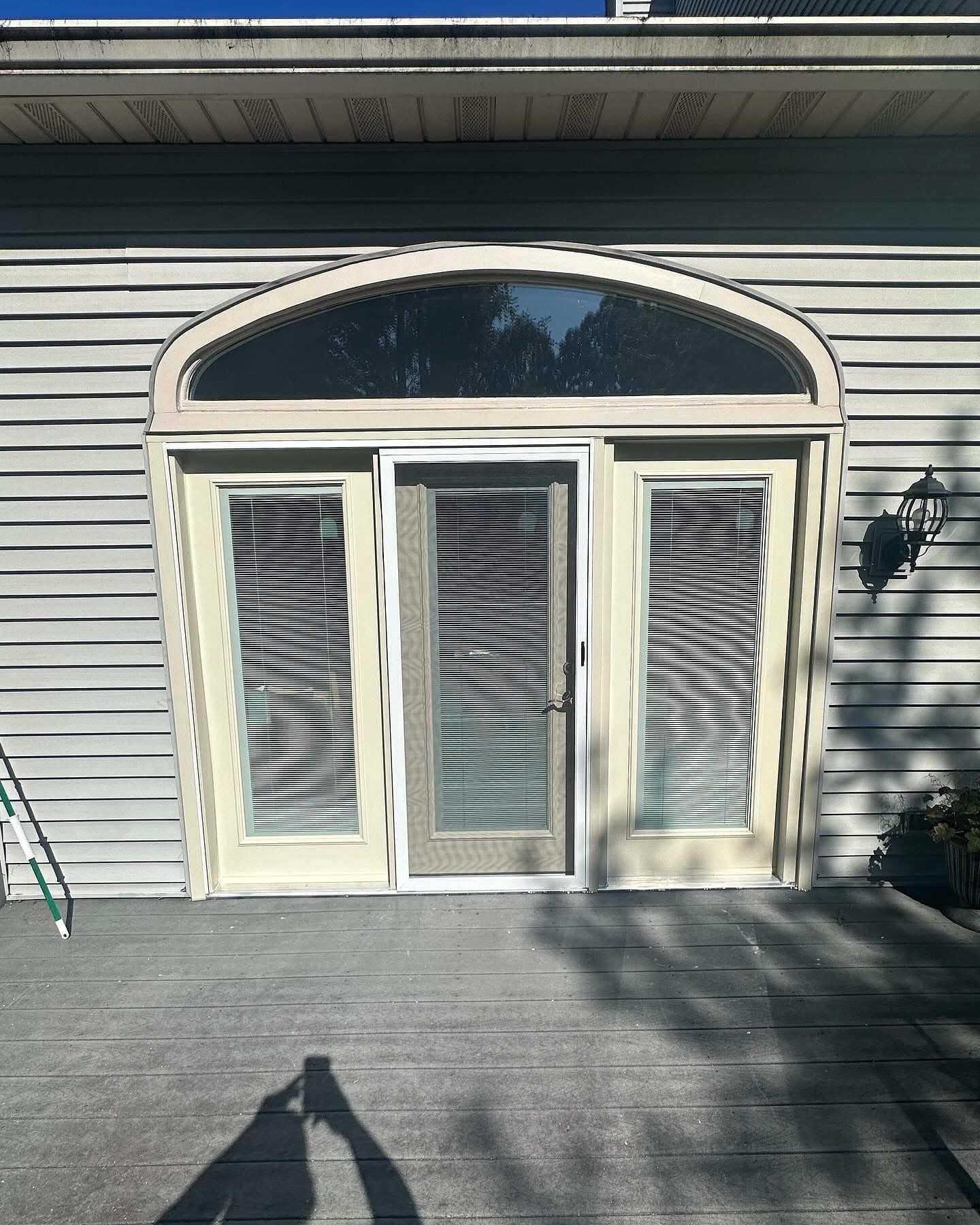 Exterior door with arched transom, surrounded by light siding.  Doors are tan with blinds, on a gray deck.