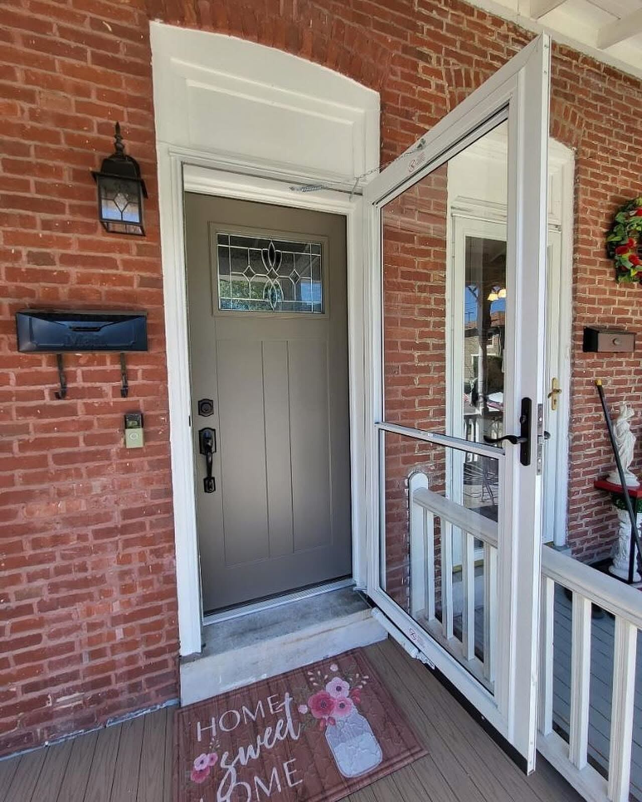 Brick entryway with a gray door, open screen door, and a welcome mat.