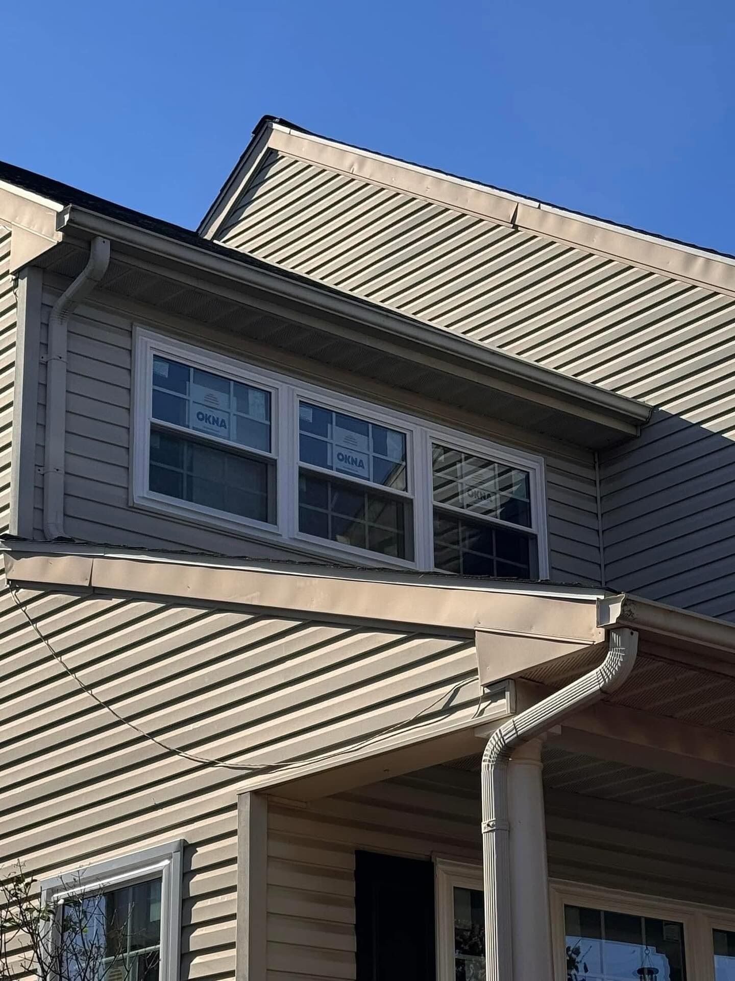 Tan house with white-framed windows, beige siding, and a blue sky in the background.