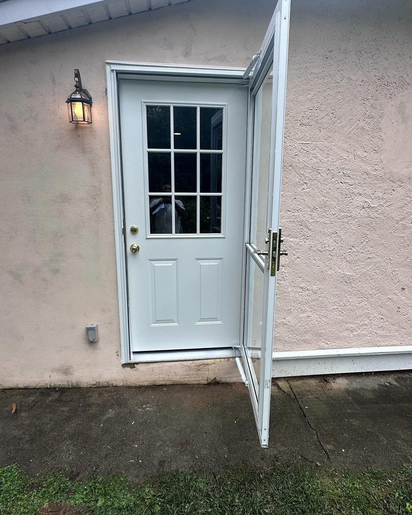White door with screen, open on a beige stucco building, with an outdoor light and concrete pad.