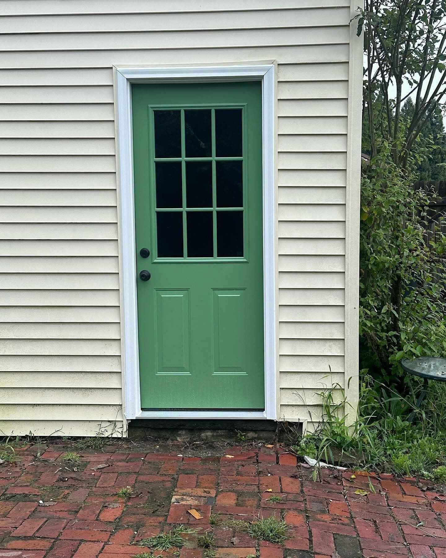 Green door with nine panes and white trim on a cream-colored building.