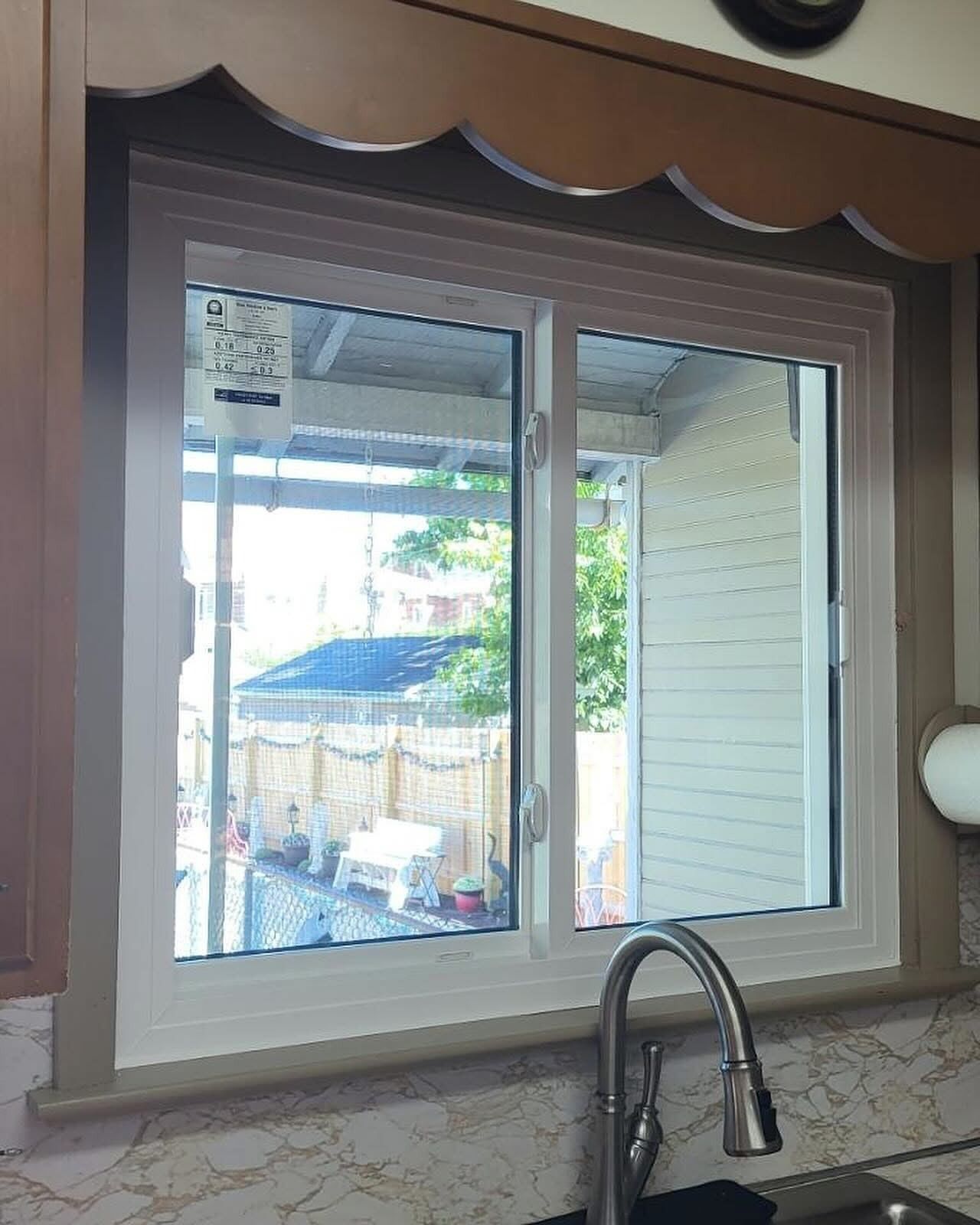 White-framed kitchen window with a view of a backyard, under a scalloped wooden valance.