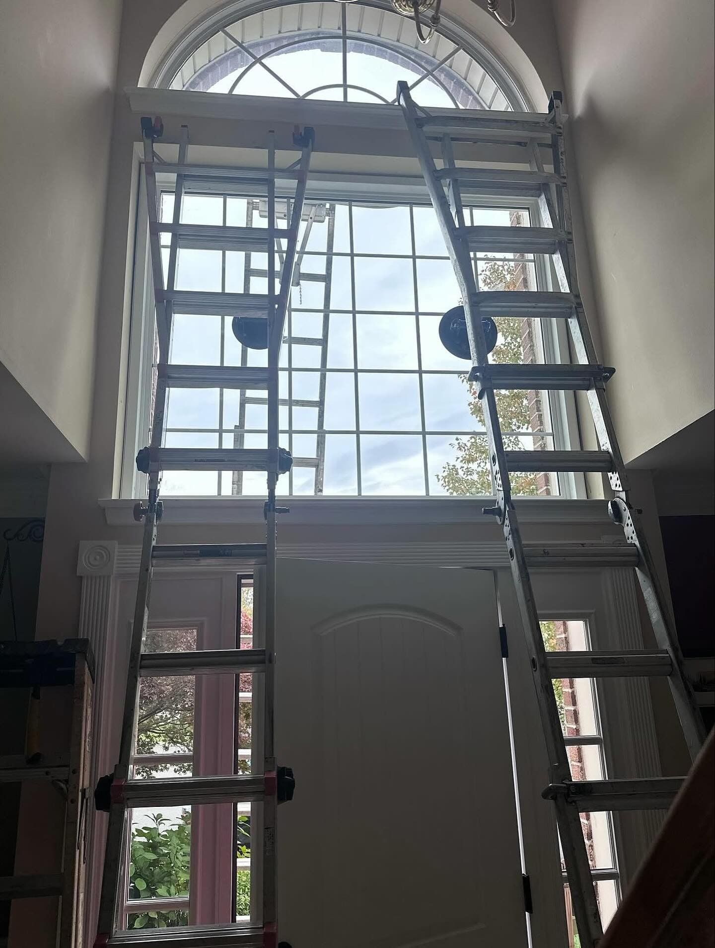 Two tall ladders propped against a large arched window for cleaning or repair.