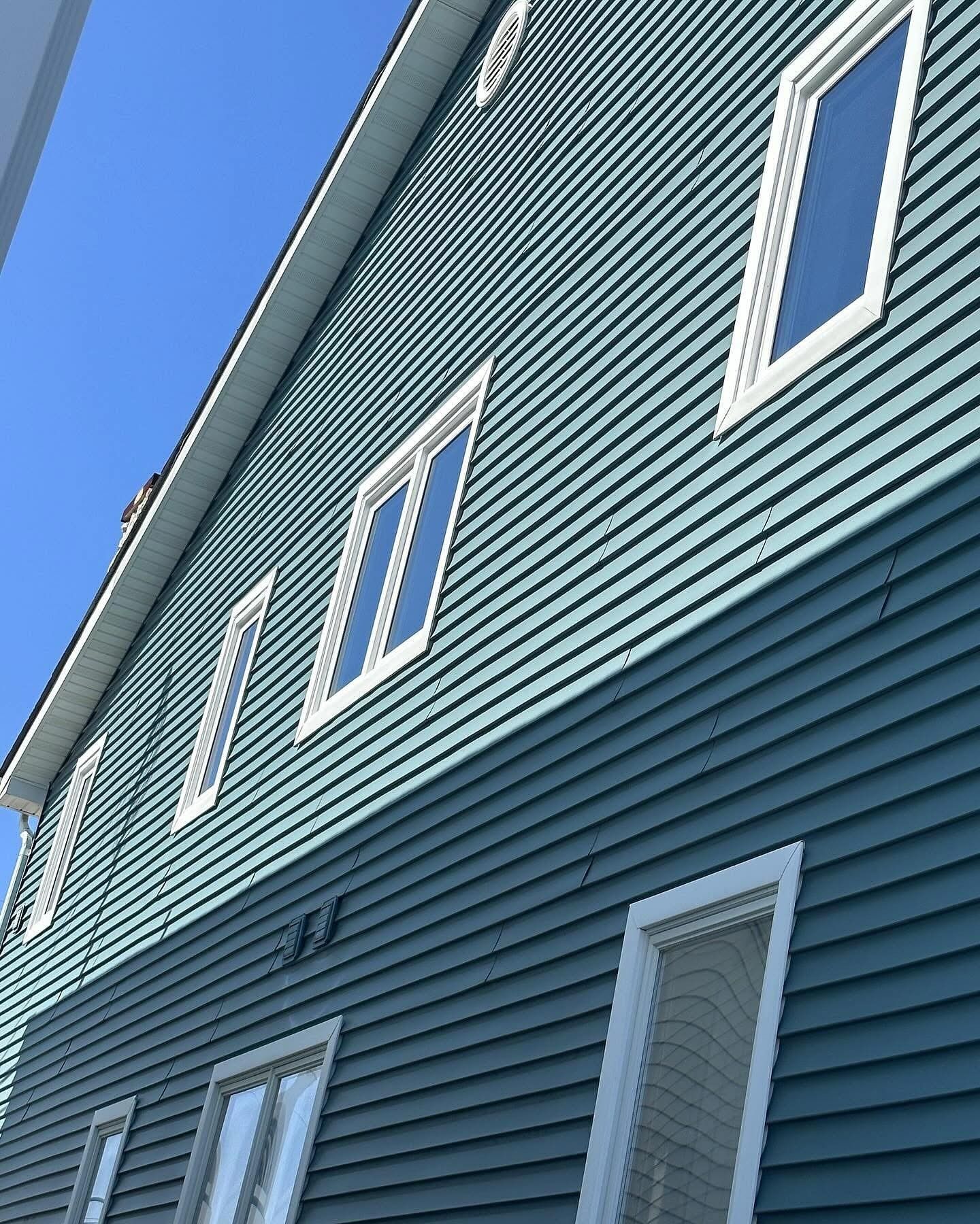 Two-story house with blue siding and white-framed windows against a clear blue sky.