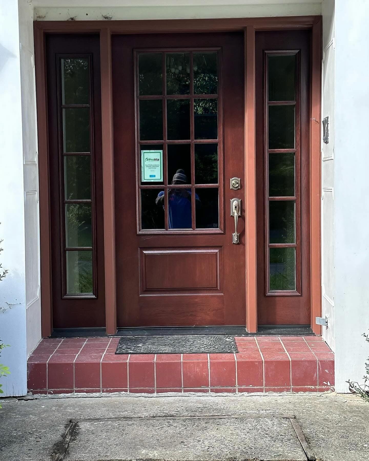 Brown front door with sidelights, red brick steps, gray walkway.