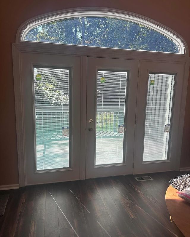 Three white French doors with a rounded top, leading outside. Dark wood floor.