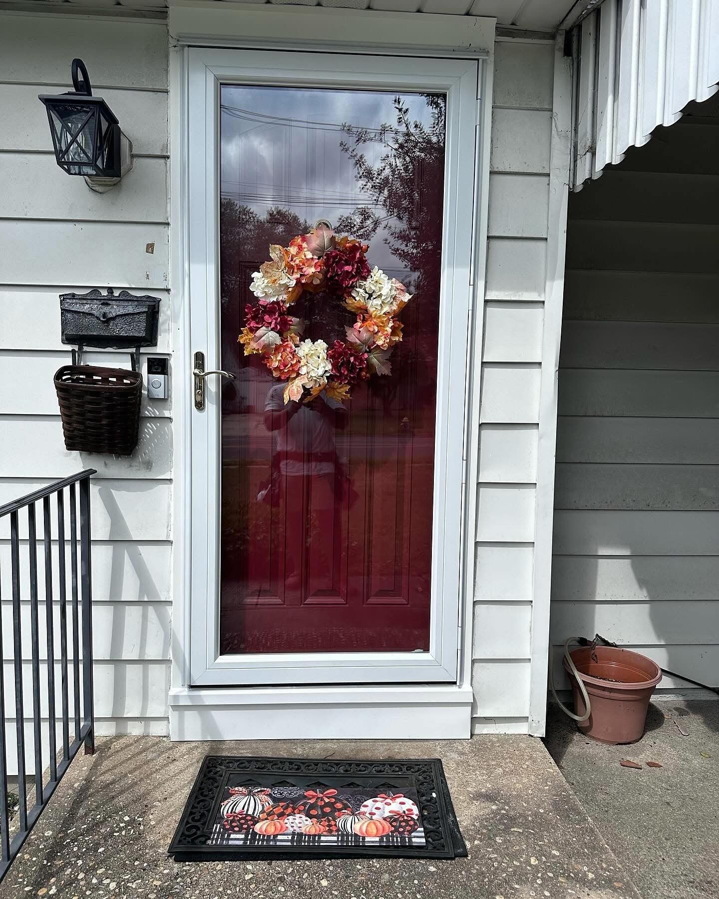Front door with wreath, storm door, welcome mat, and mailbox.