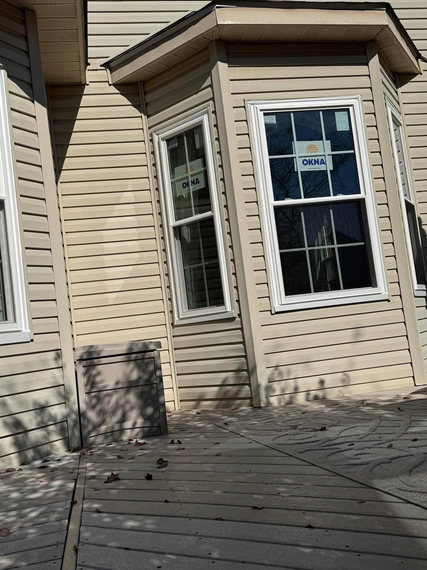 Beige siding on a house with a bay window and a wooden deck. The windows have white trim.