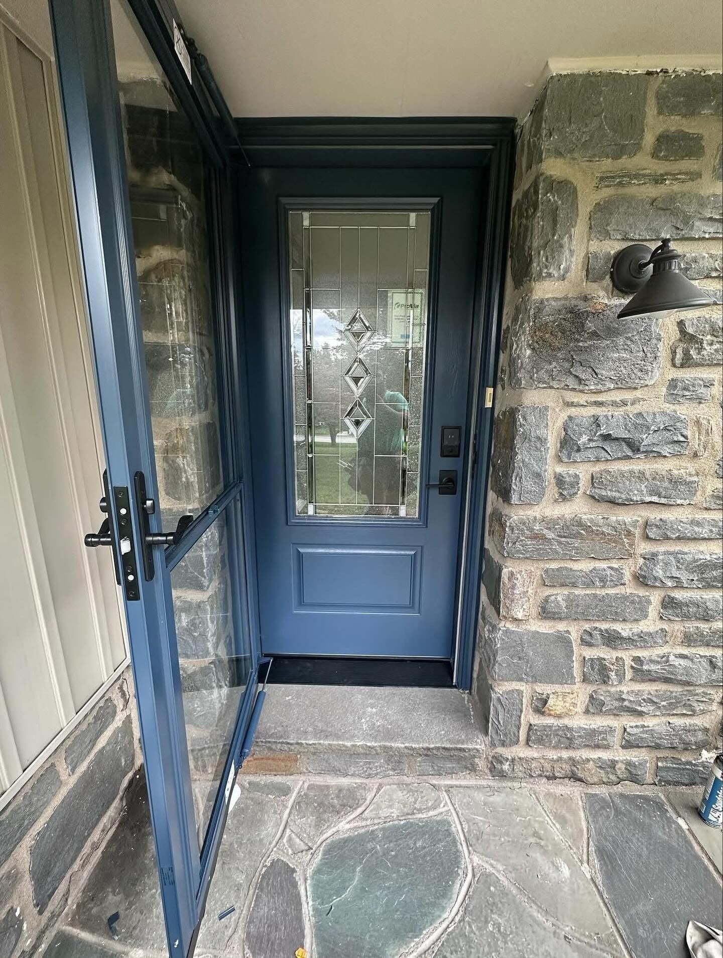 Blue front door with glass panel and storm door on a stone exterior.