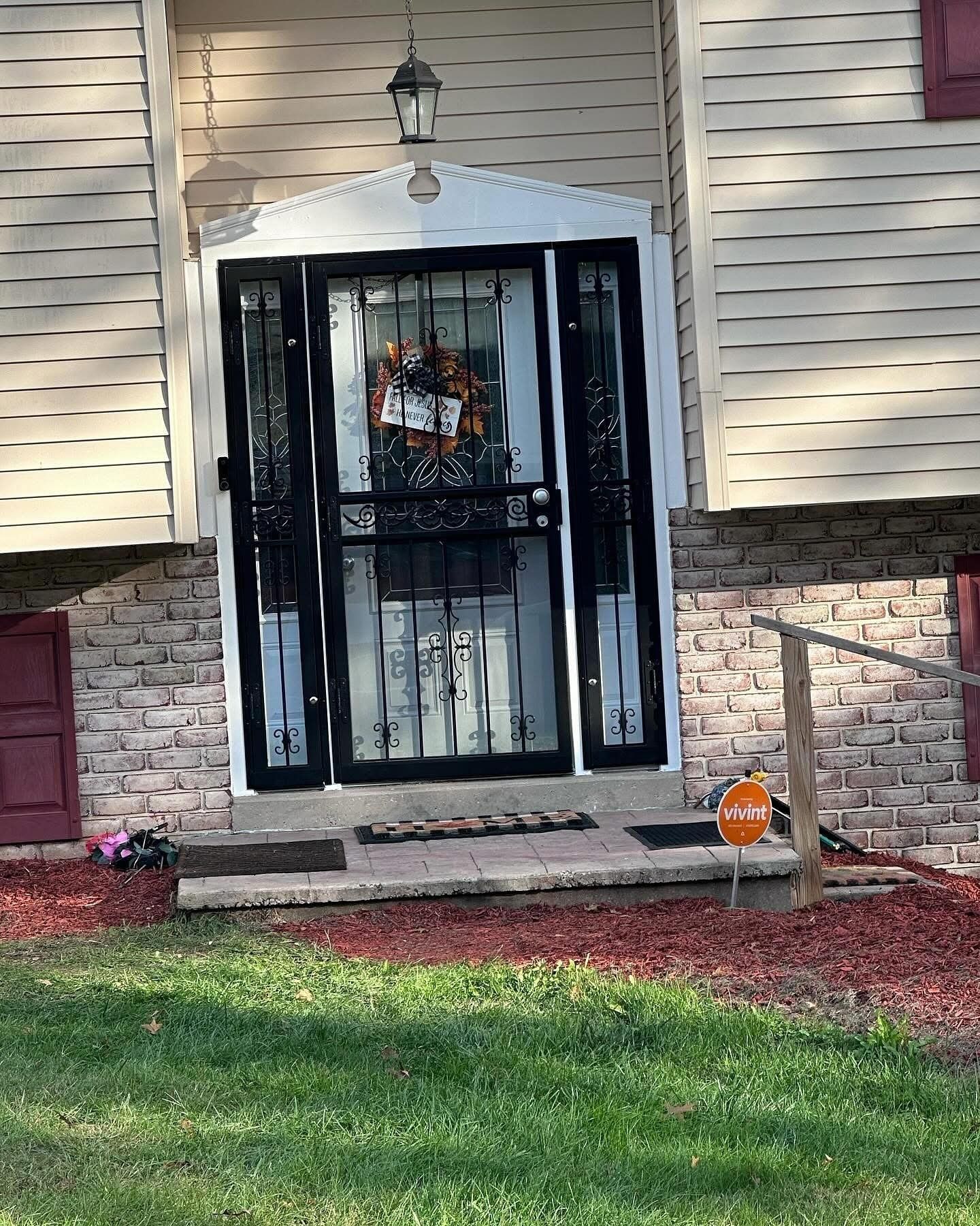 Front entrance of a house. Black security door with decorative glass, and a door mat. A wreath hangs on the door.