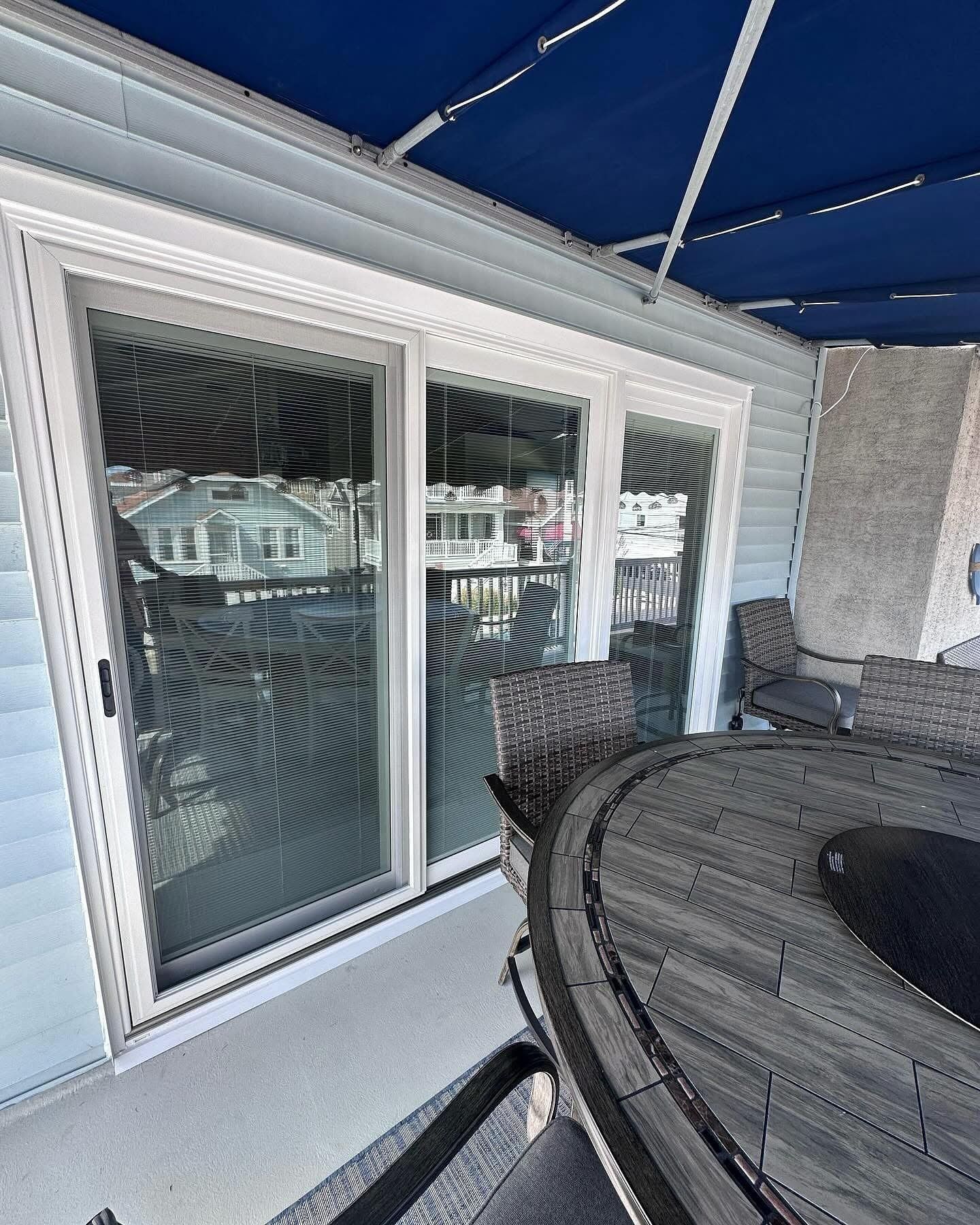 Sliding glass door on a porch, blue awning, wicker furniture, round table, houses in the background.