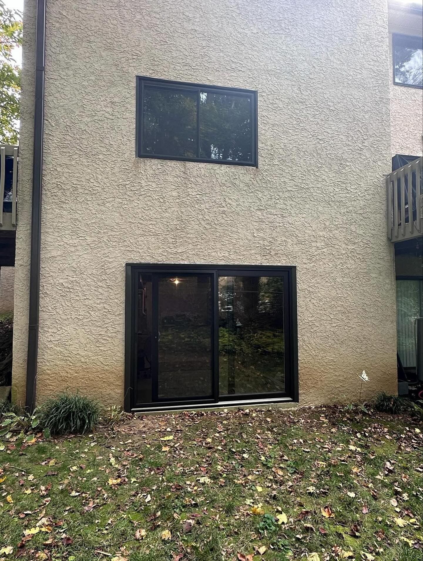 Exterior of a building with a window above a sliding glass door. The textured wall is beige.