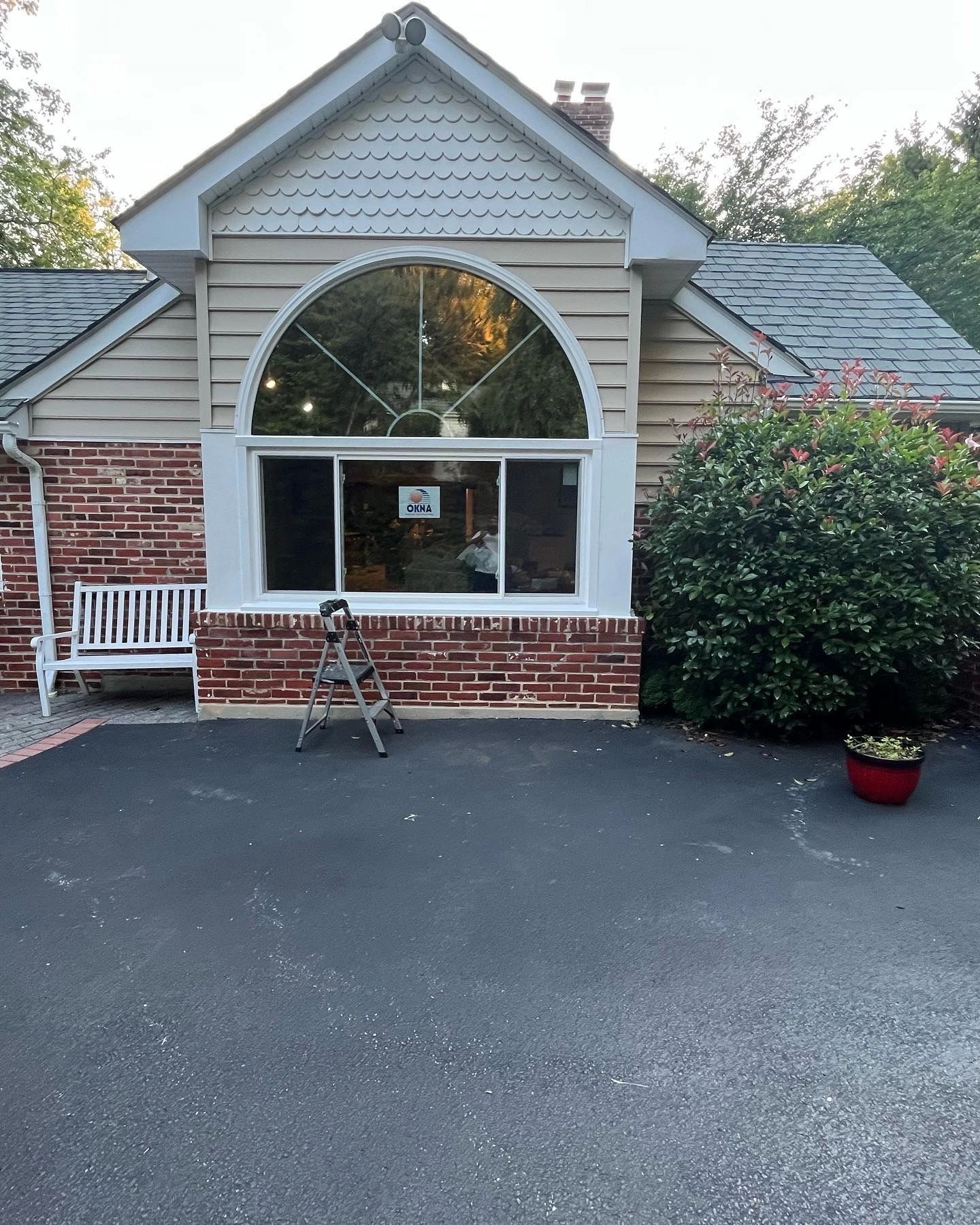 Dog stands in front of a brick building with a large arched window. A bench and bush are visible.