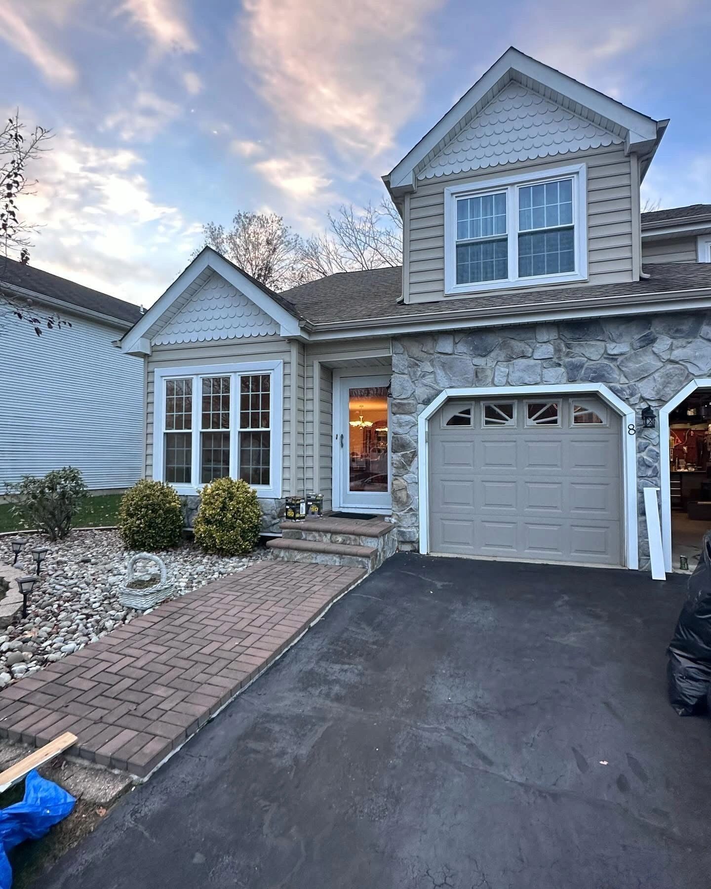 Two-story house with stone and beige siding, driveway, and paved walkway, with a cloudy sky in the background.