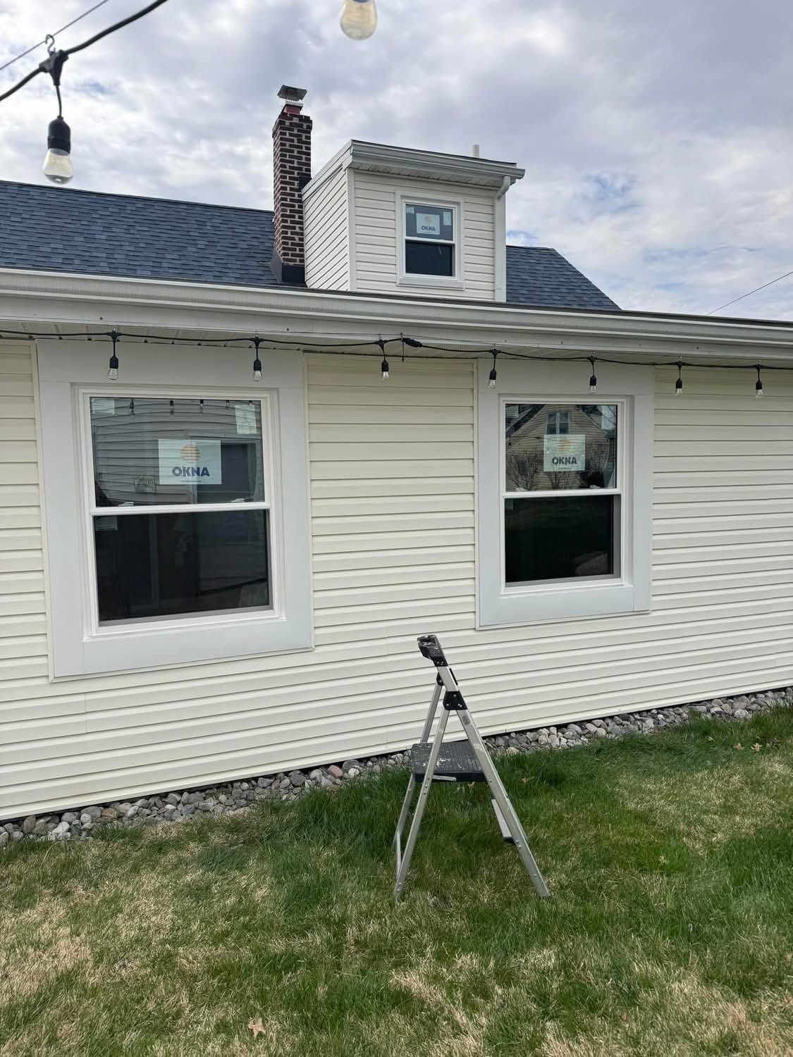 Exterior view of a house with white siding and new windows. A small dormer and chimney are visible on the roof.