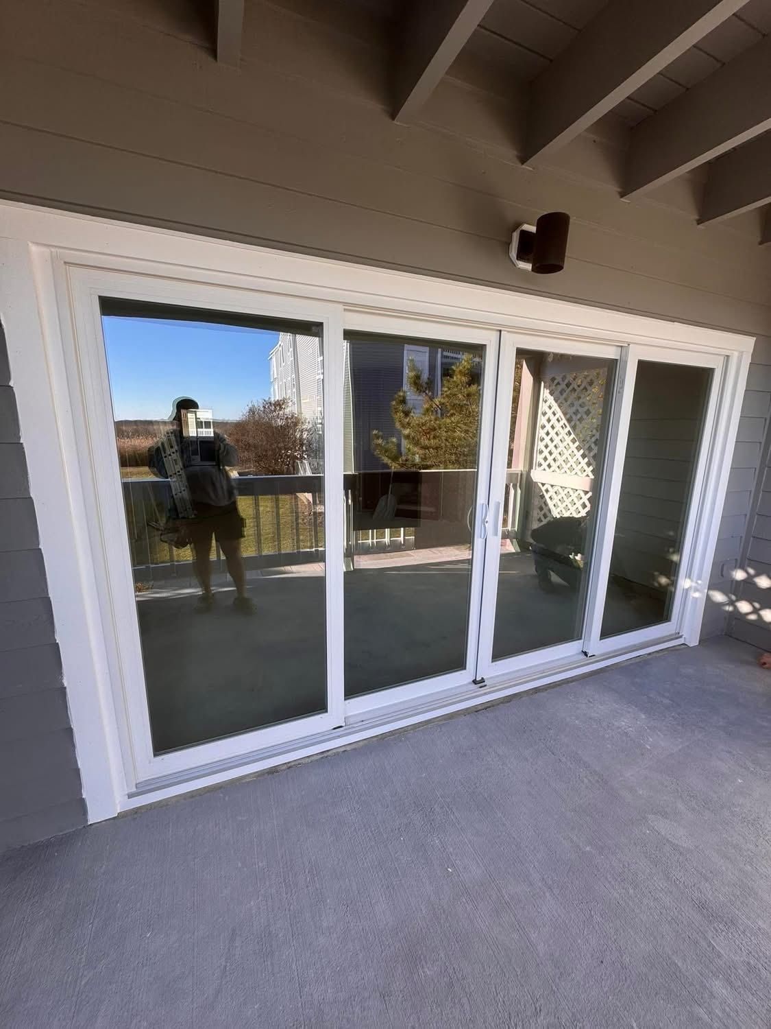 Sliding glass doors with white frame, reflected person taking photo, gray exterior.